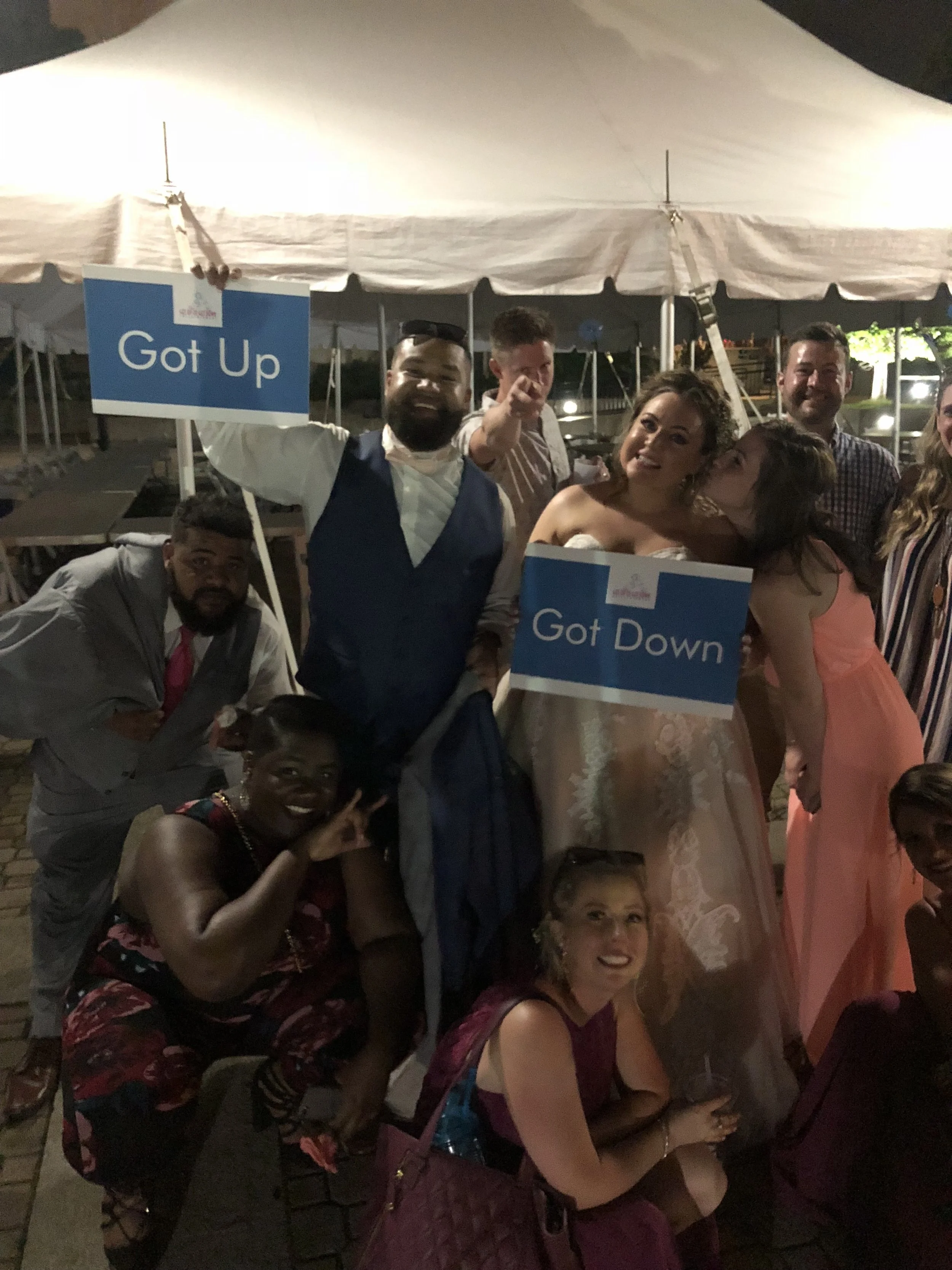 Wedding guests holding Got Up and Got Down signs beneath a reception tent at the Botanical Gardens.