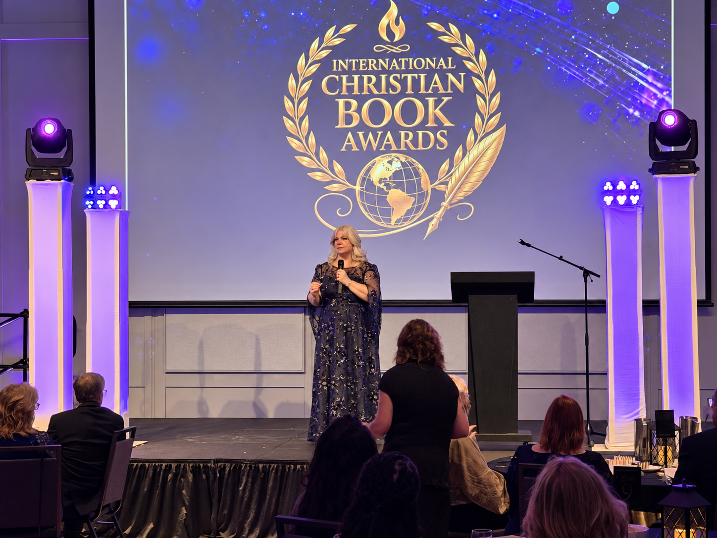Stage lighting and projection frame a speaker at the International Christian Book Awards gala.