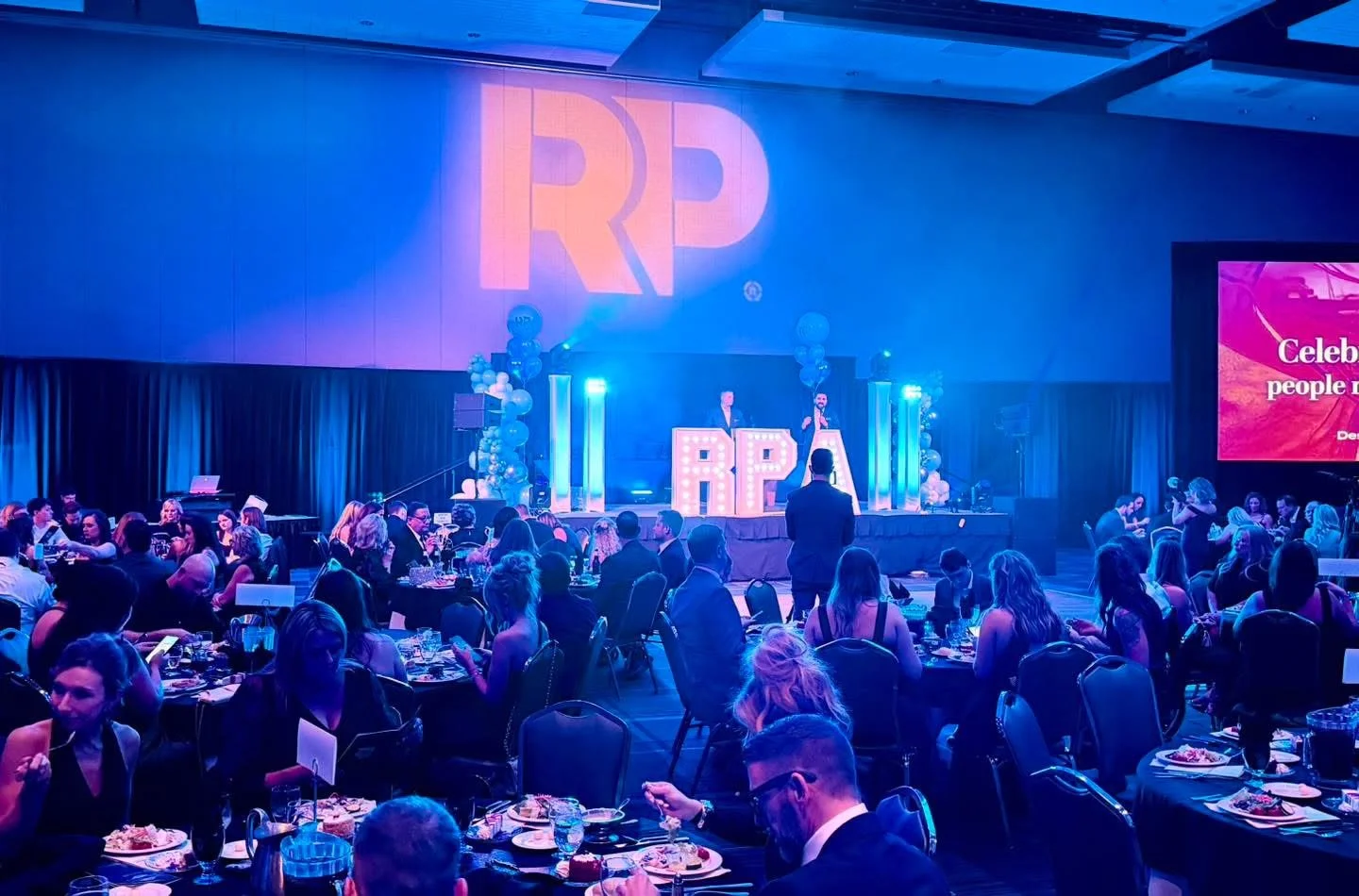 Blue lighting fills the room at the Real Producers Gala and Awards Ceremony, with illuminated stage columns and projected RP branding.
