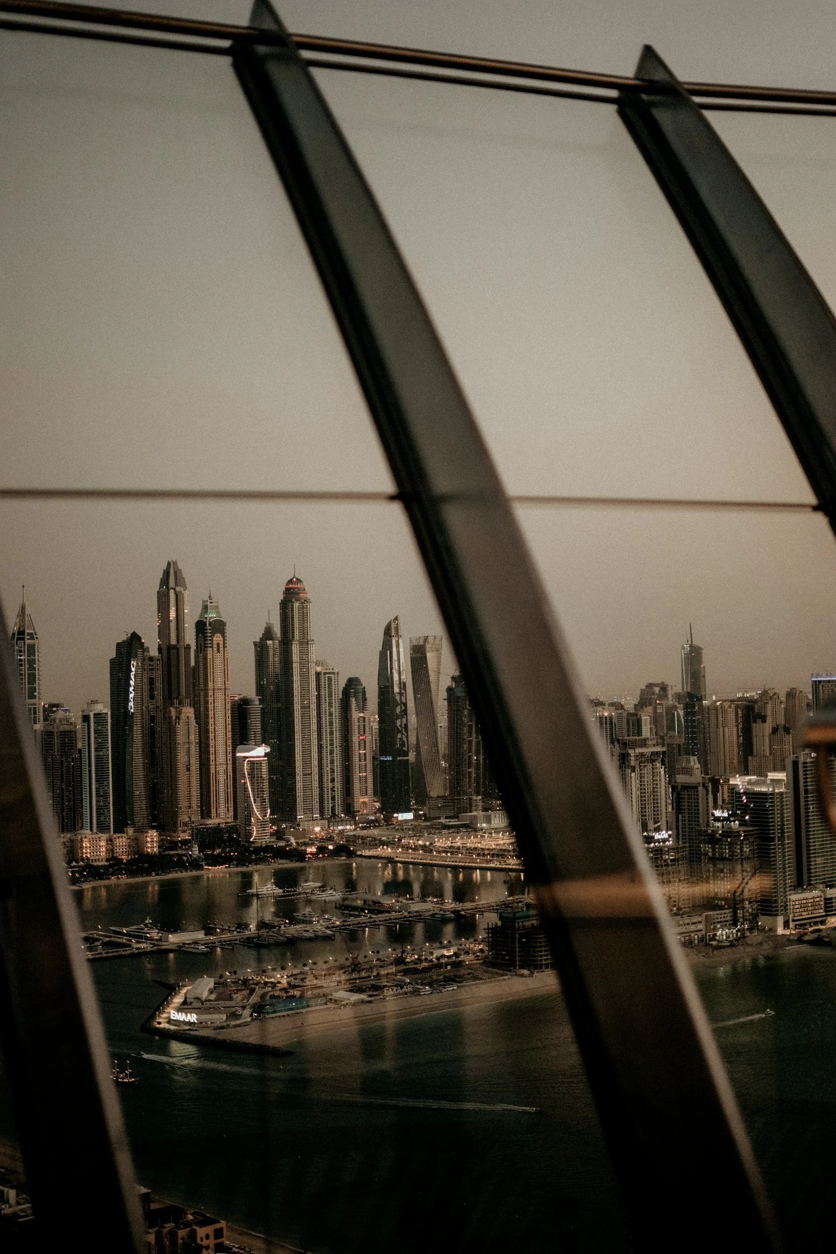 A city skyline with numerous tall skyscrapers visible through a window with curved black frame parts in the foreground.