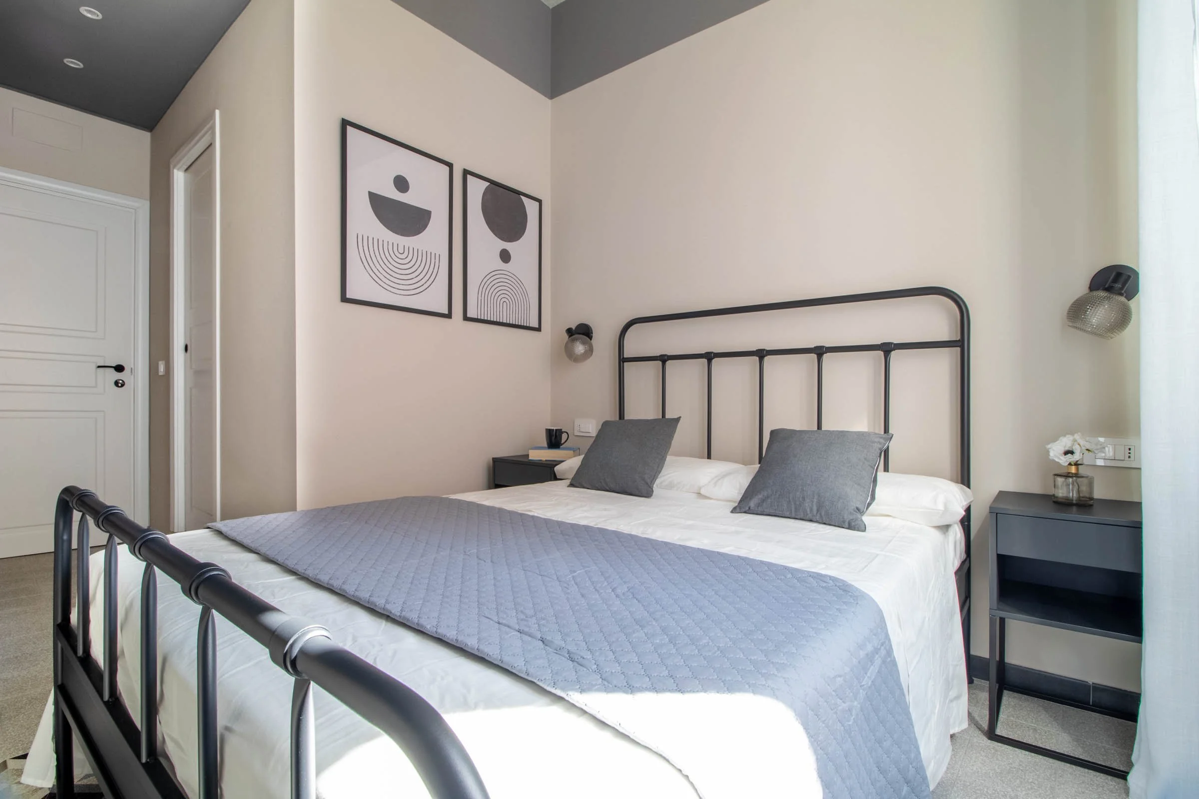 Una camera da letto moderna con un letto con quadri grigi, due appoggi di notte grigi, e decorazioni minimaliste alle pareti.