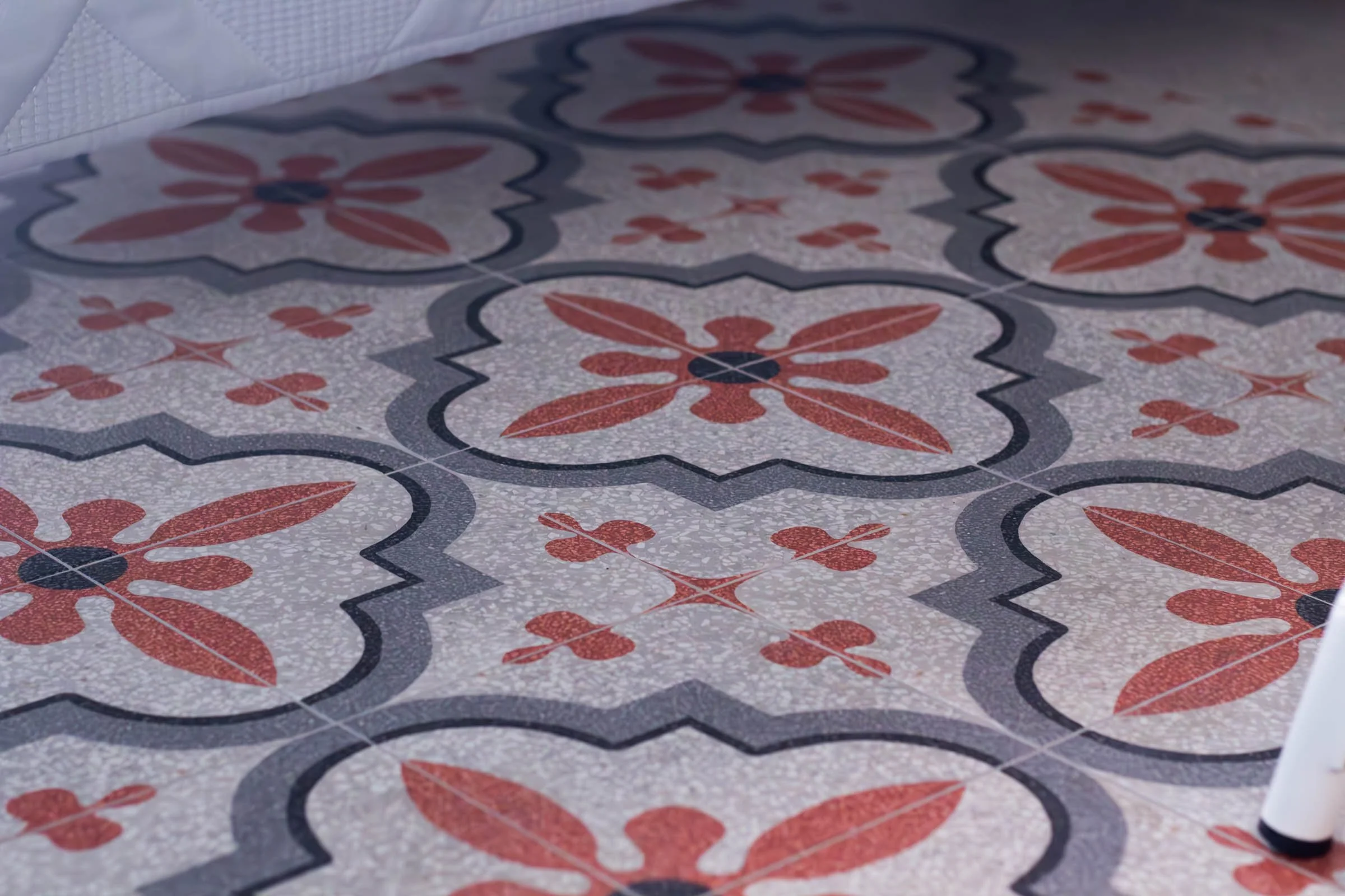 Piastrelle decorative con motivi floreali e geometrici in colori rosso, nero e grigio, con un bordo bianco sul lato superiore dell'immagine.