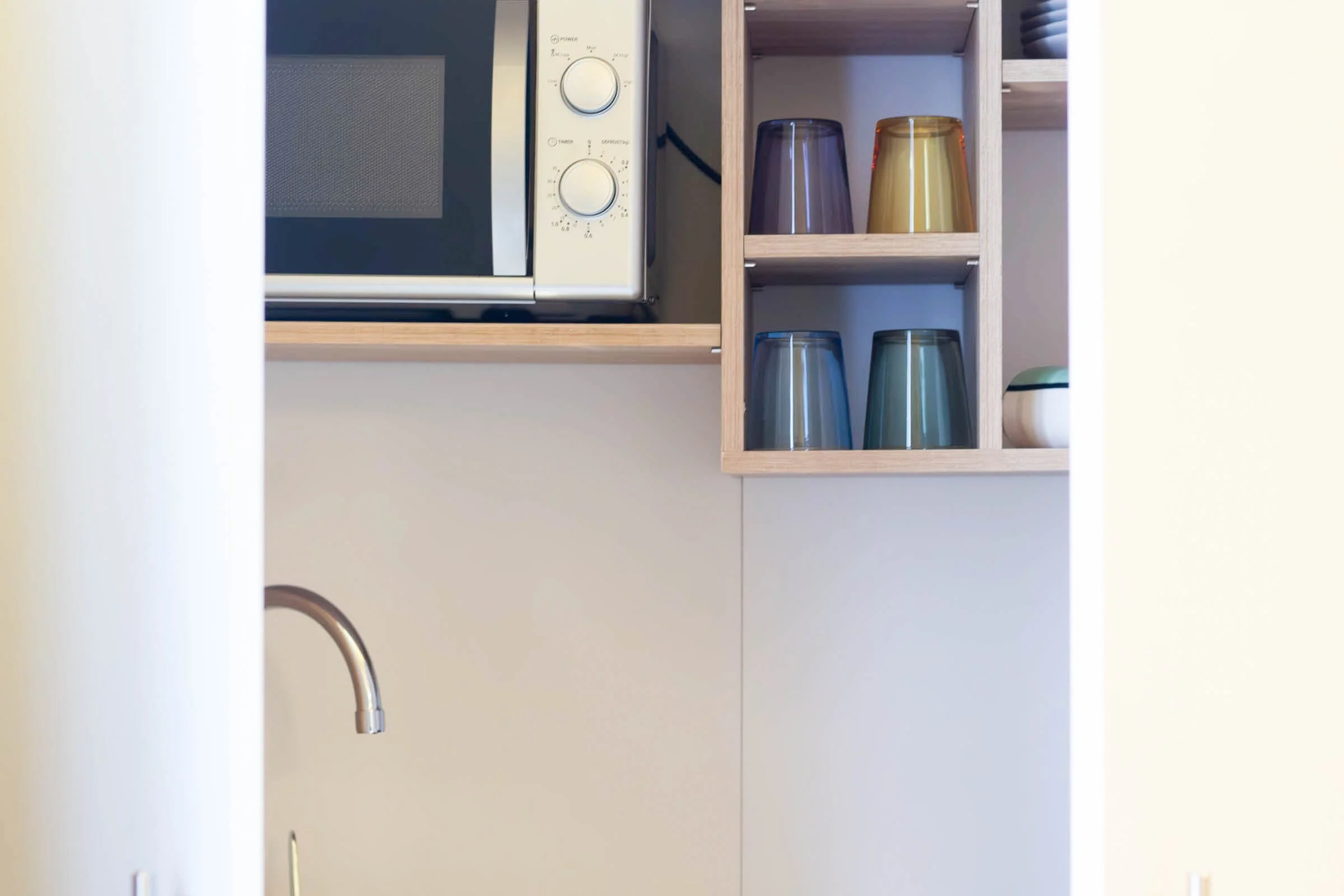 Gestore di cucina con microonde e bicchieri colorati su uno scaffale di legno.