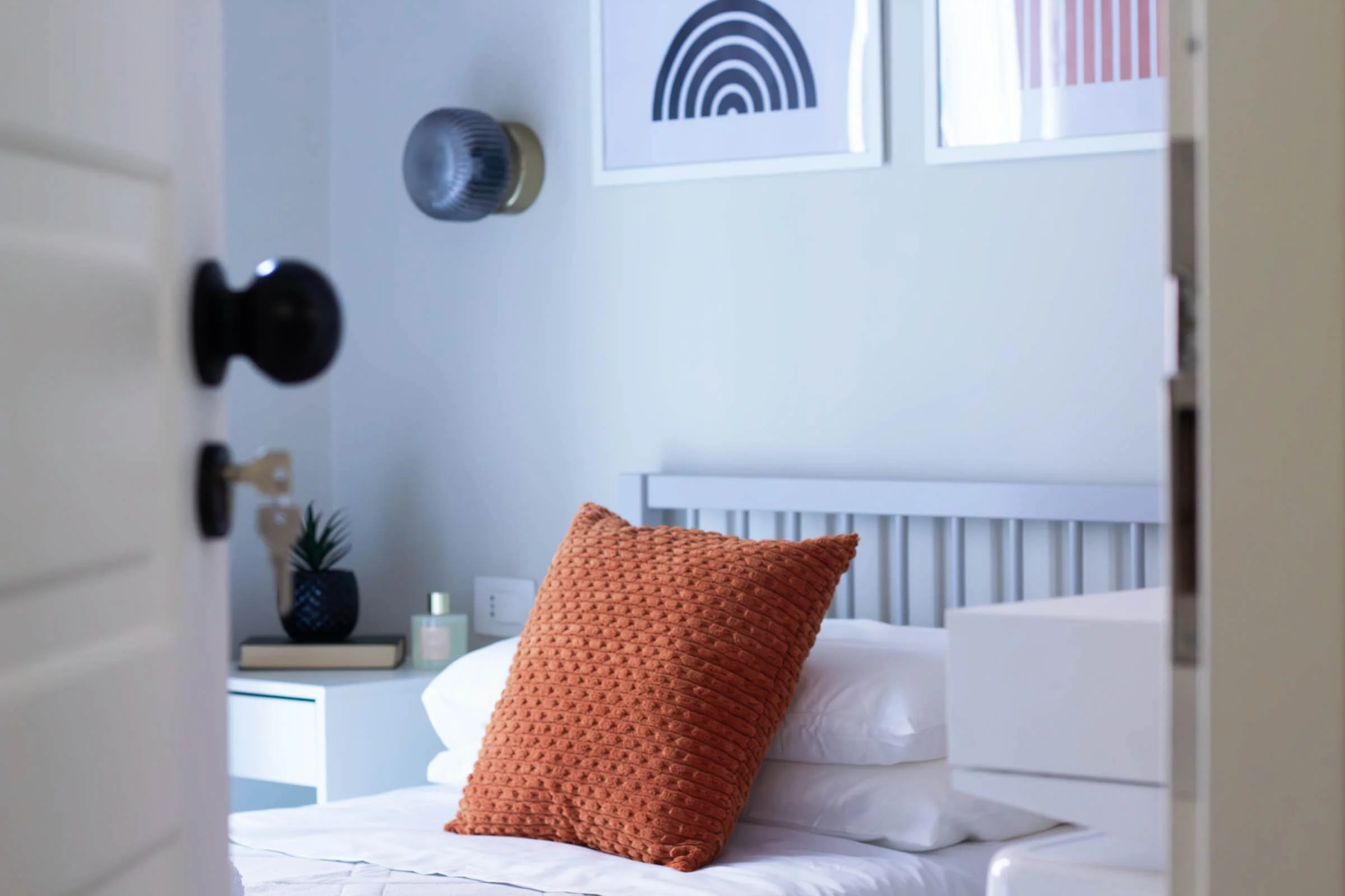 Letto con due cuscini arancioni cuciti a maglia in una stanza moderna, vista parziale dell'ingresso
