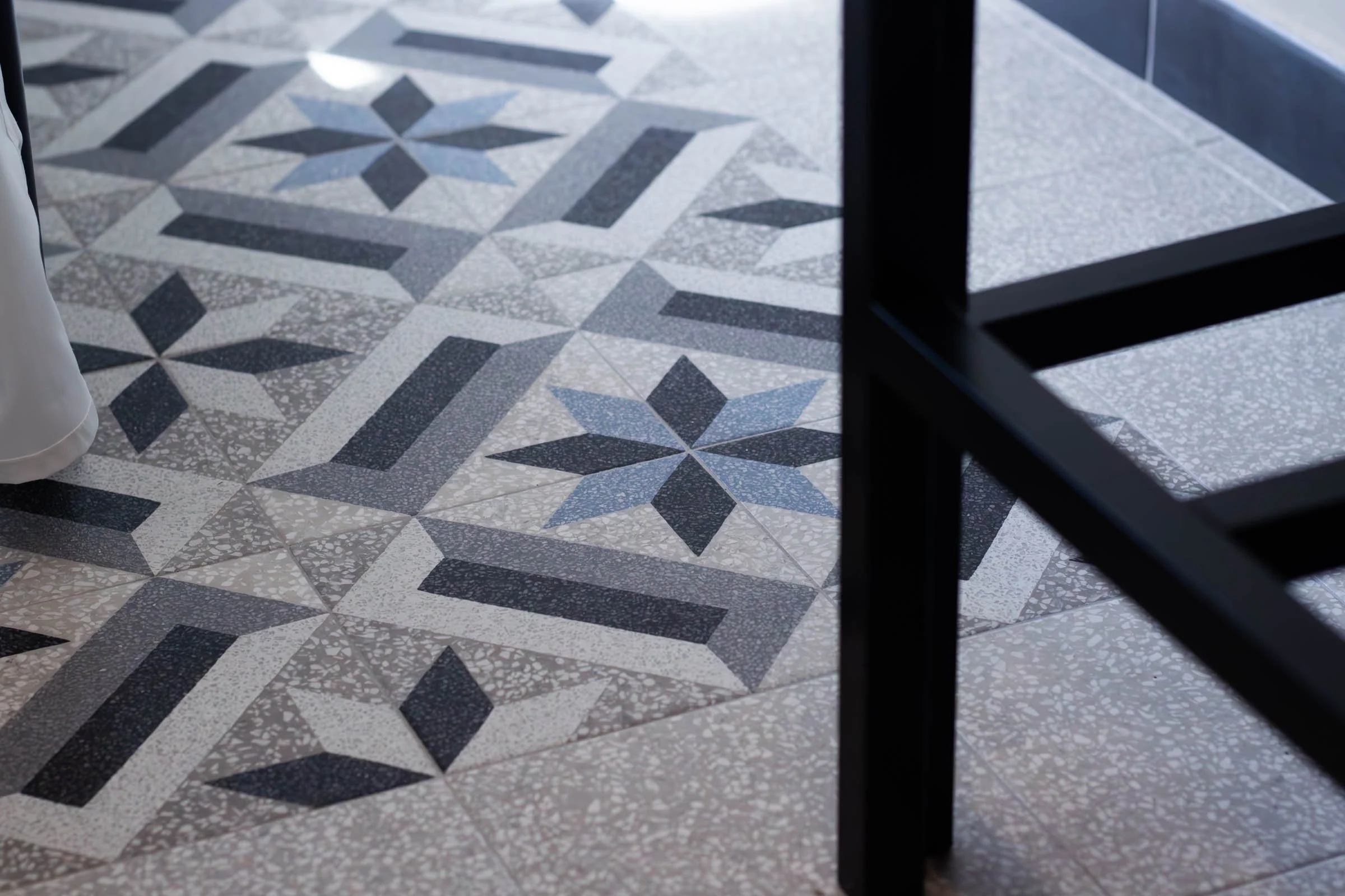 Piastrelle decorative in ceramica con motivo geometrico blu e grigio, viste parzialmente attraverso una ringhiera nera.