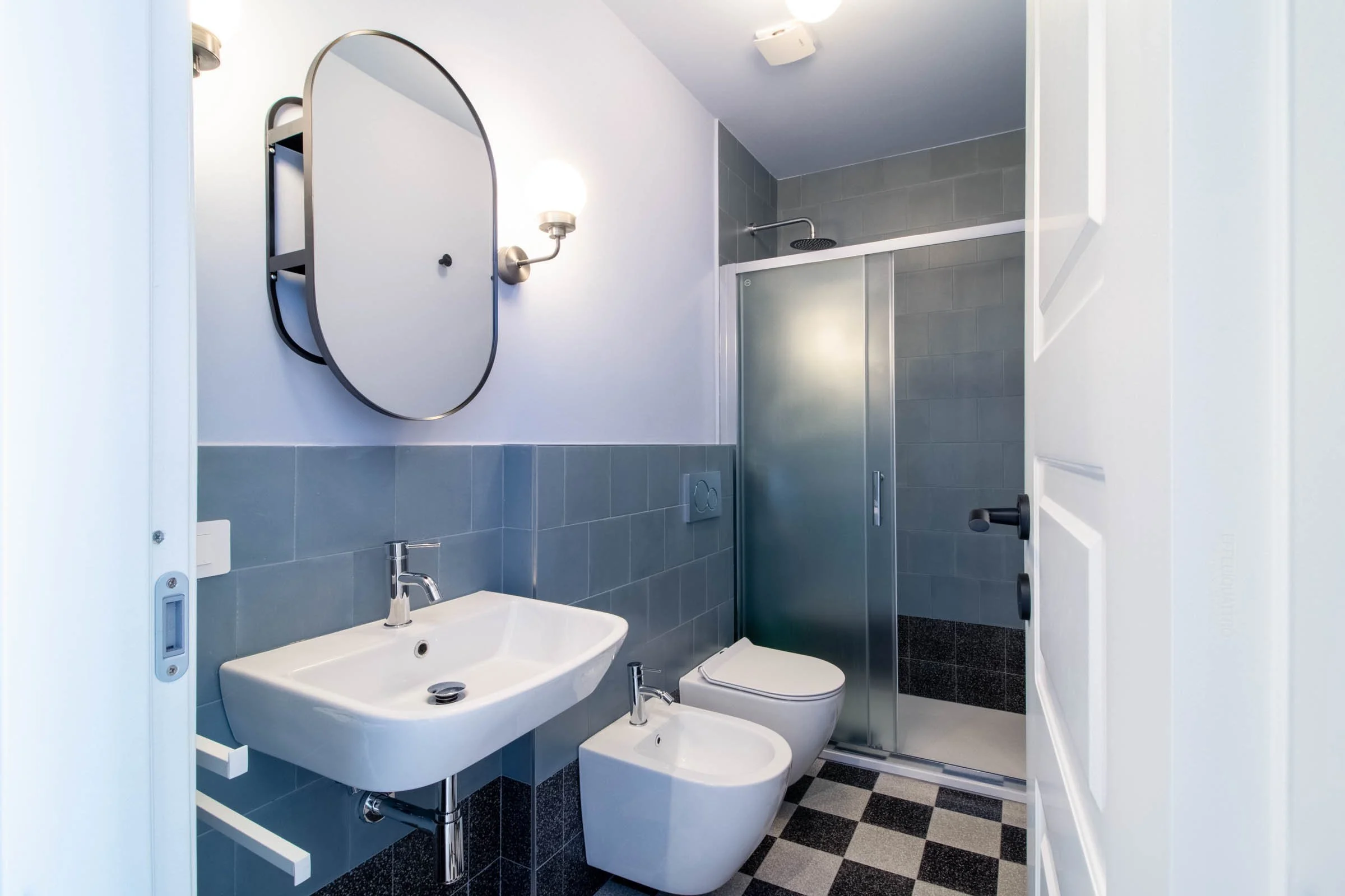 Bagno con lavabo, bidet, WC e doccia separata, pareti e pavimento in piastrelle di colore grigio e bianco.