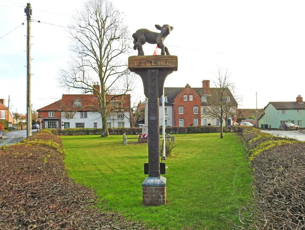 A sculpture of a pig on a tall pedestal in a town square, with houses and leafless trees in the background.
