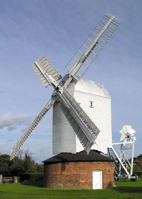 A traditional white windmill with four blades, situated on a brick base, against a partly cloudy blue sky.