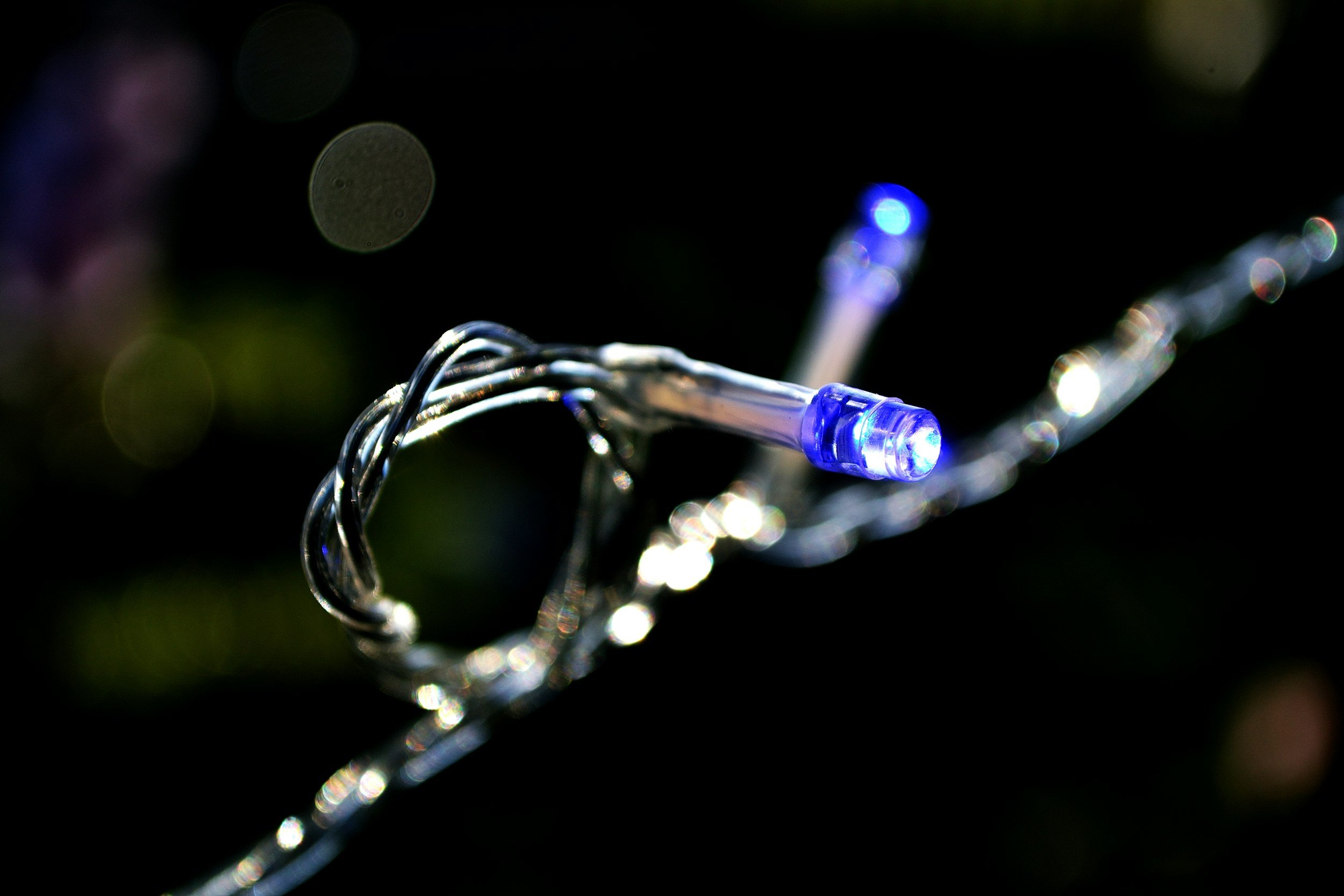Close-up of a string of LED lights with a blue and white glow, decorated with metallic wire, against a dark background.