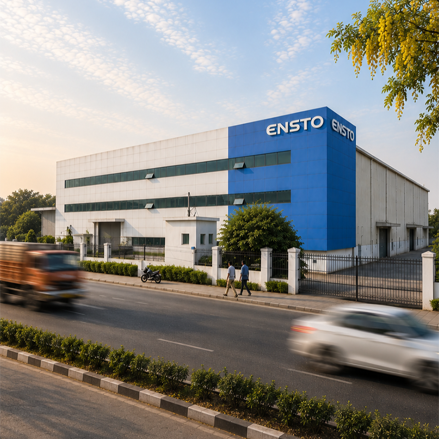 Commercial building with the sign 'ENSTO' on the front and side, situated along a busy road with cars and pedestrians, under a blue sky with scattered clouds.