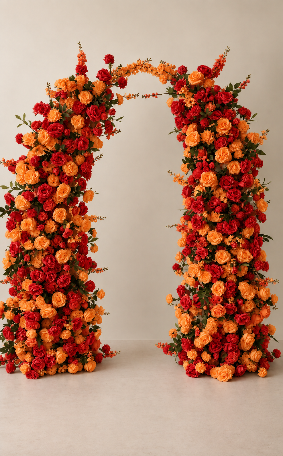 A large floral arrangement with red and orange roses and other flowers arranged in an arch shape against a plain background.