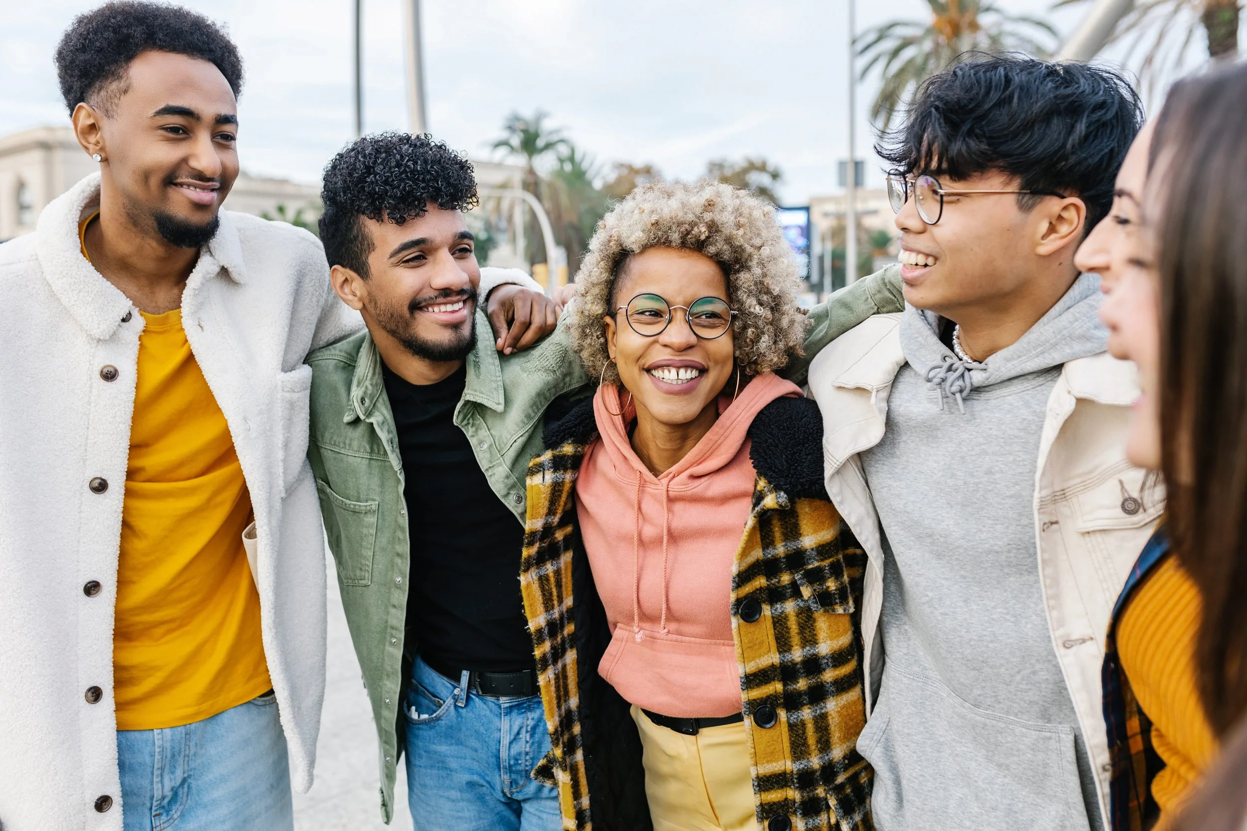 A diverse group of friends standing close together outdoors, smiling and enjoying each other's company.