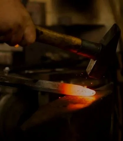 A blacksmith heating a piece of metal in a forge with a hammer nearby.