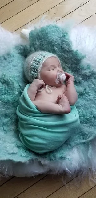 Newborn baby wrapped in a soft green blanket, representing the personal inspiration behind Bri Bear Care.