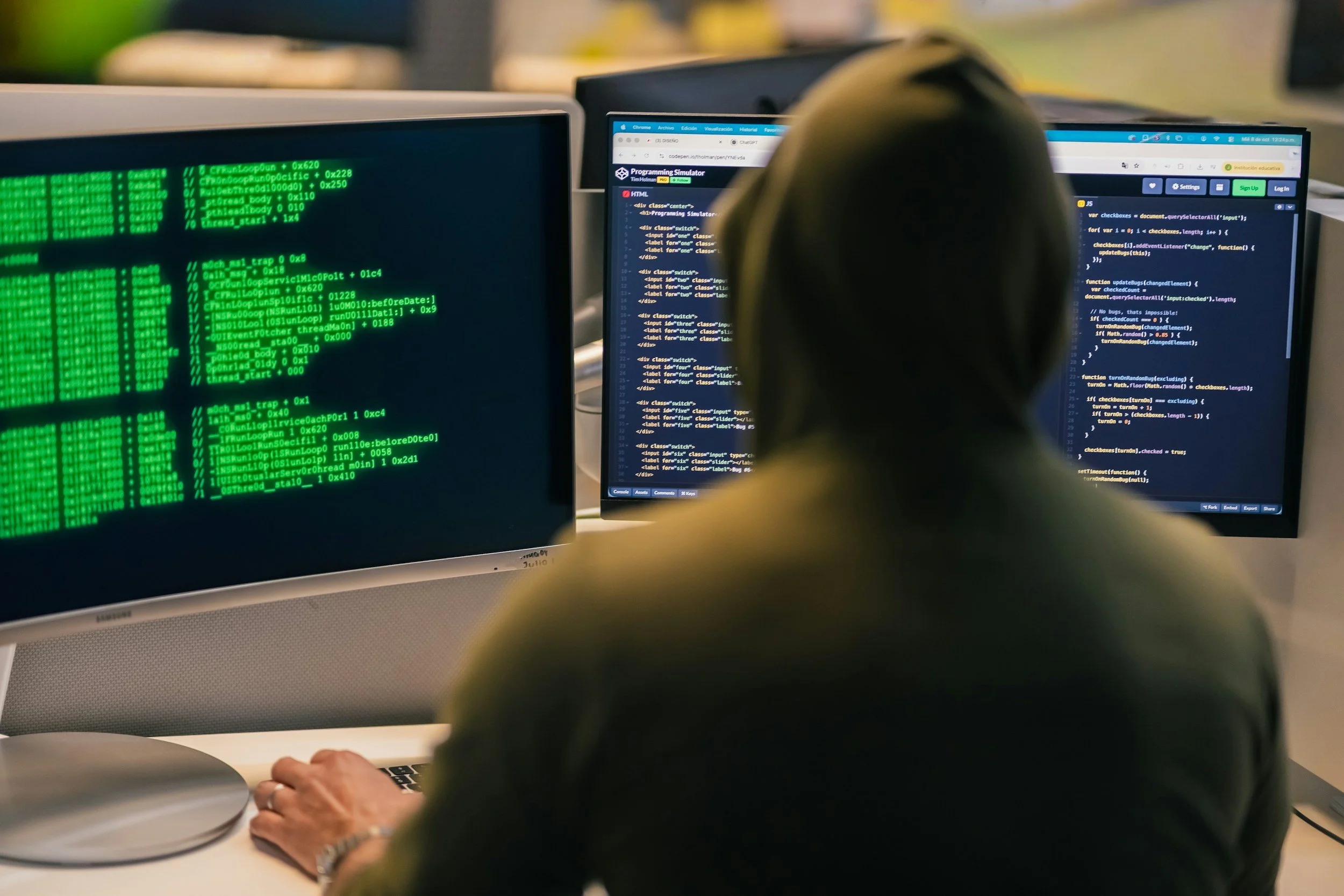 Person working at a computer with two monitors, one displaying green computer code and the other showing a programming simulation interface.