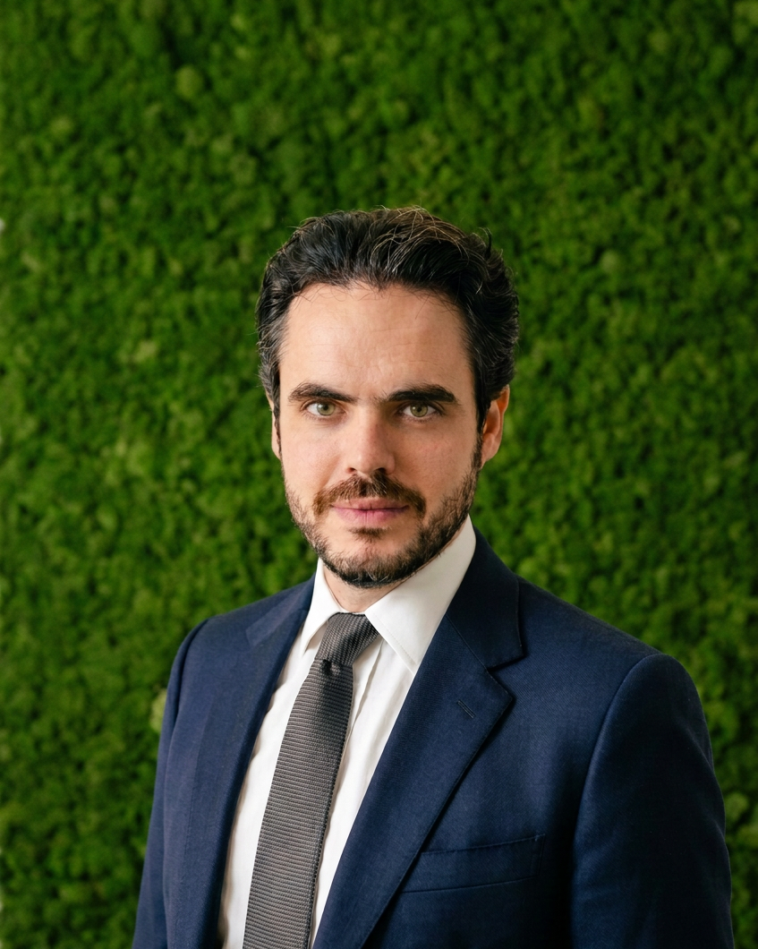 Professional man in a suit and tie against a green hedge background.