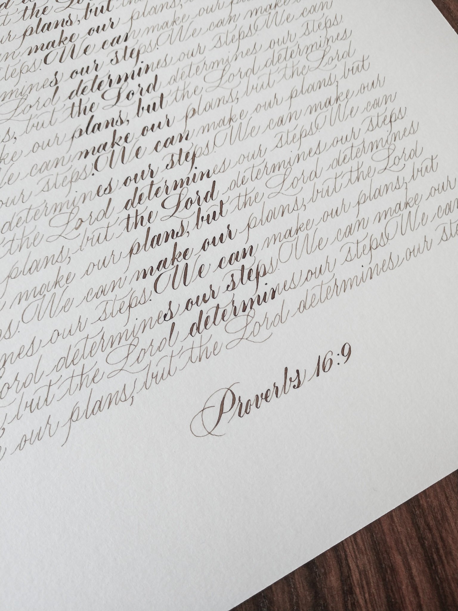 Close-up of a handwritten scripture passage in elegant cursive writing on white paper, with a wooden surface in the background.