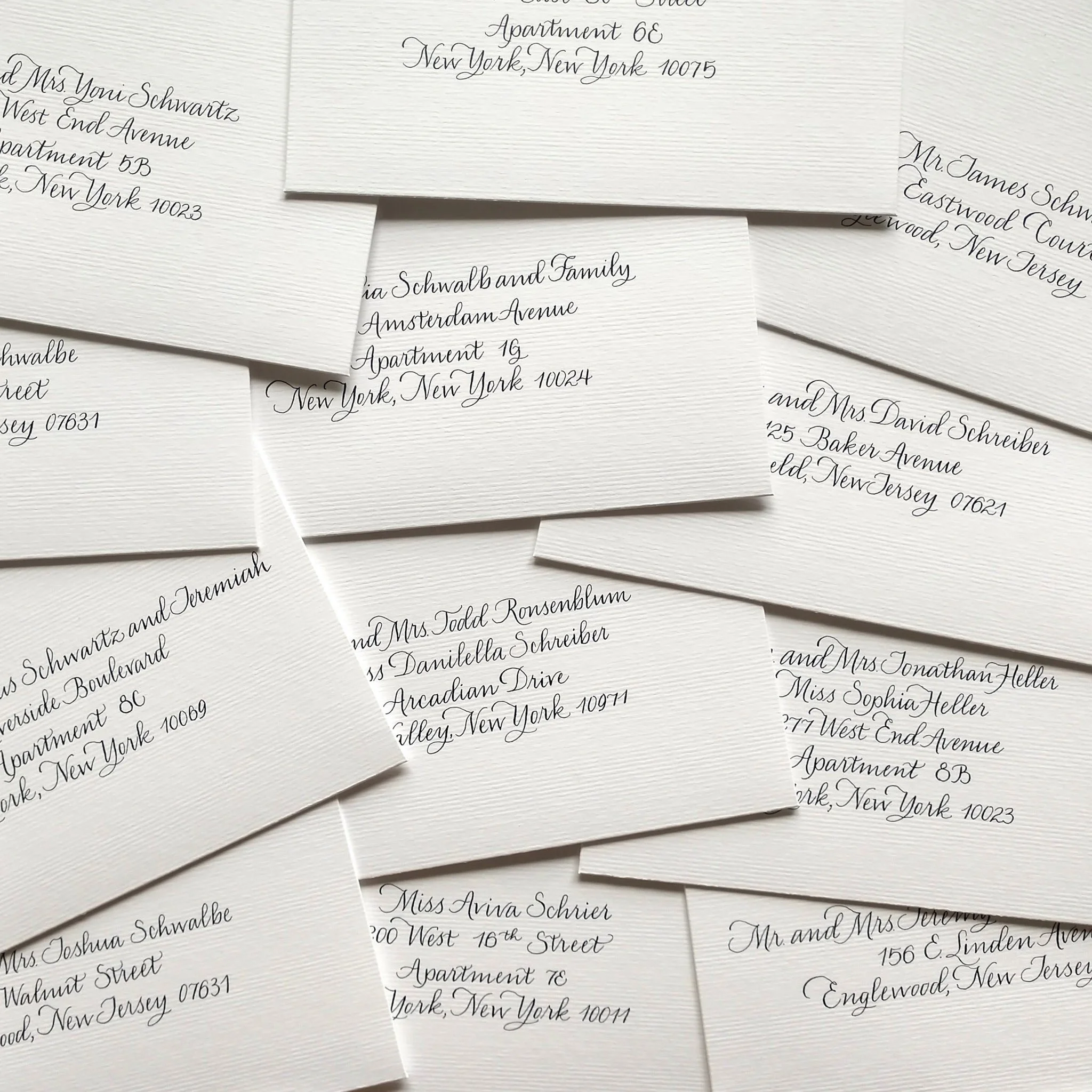 Multiple white wedding envelopes with elegant black cursive addresses layered on top of each other.