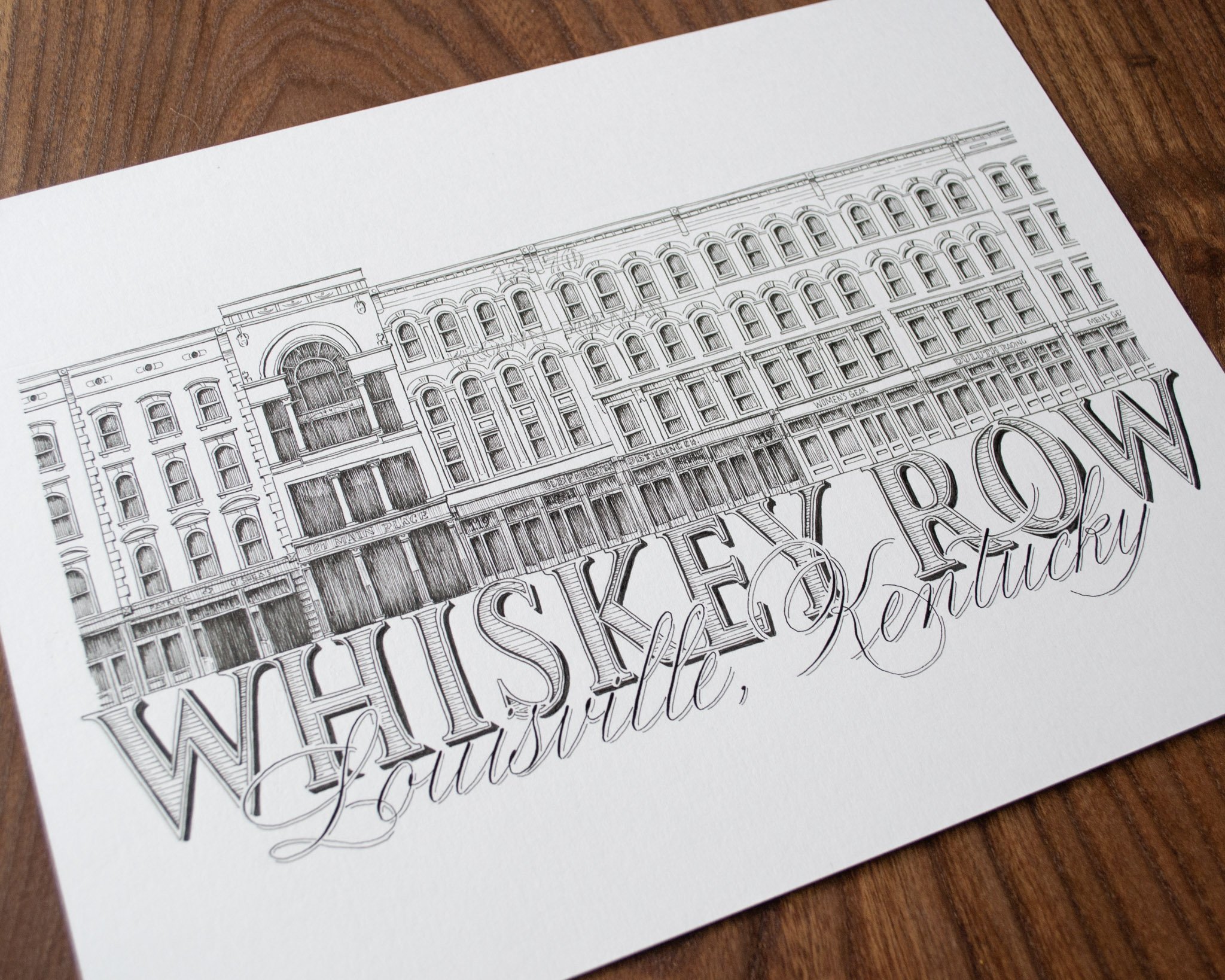 A detailed architectural sketch of a multi-story building with ornate windows and decorative elements, involving precise line work on white paper, placed on a wooden surface.