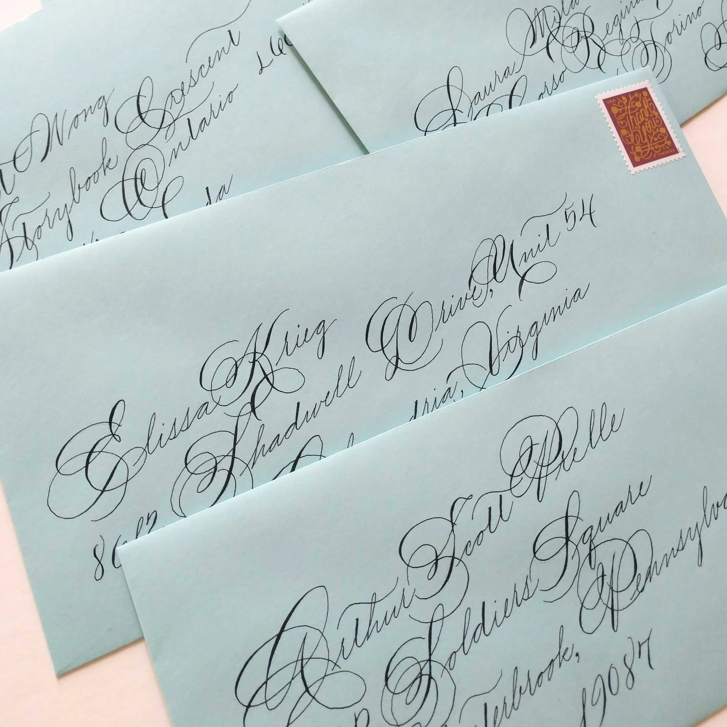 Close-up of light blue handwritten letters on light blue paper with elaborate cursive script, overlapping and partially obscured, with a red and pink postage stamp in the top right corner.