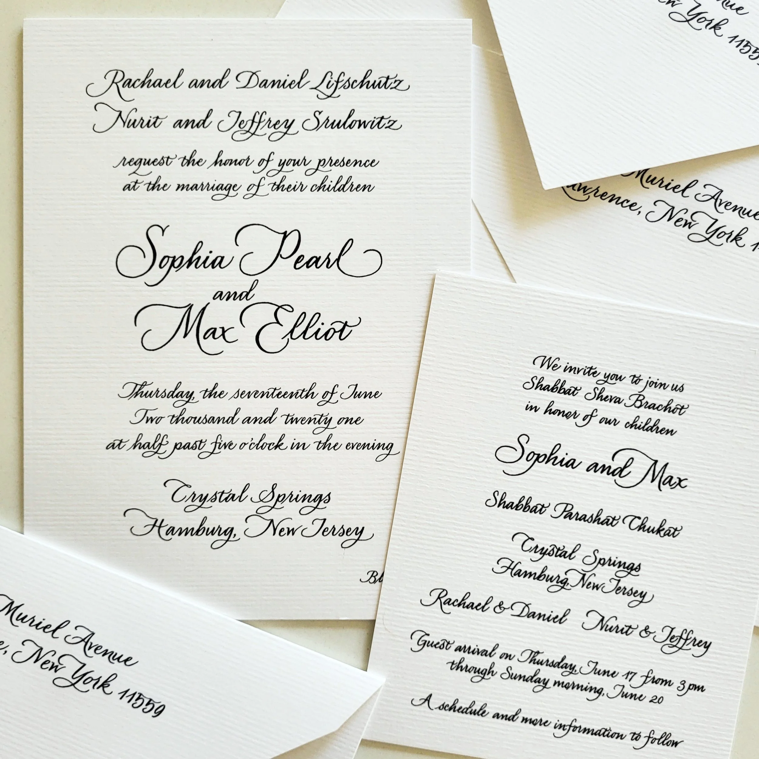 Close-up of elegant wedding invitation cards with black cursive text on white textured paper.