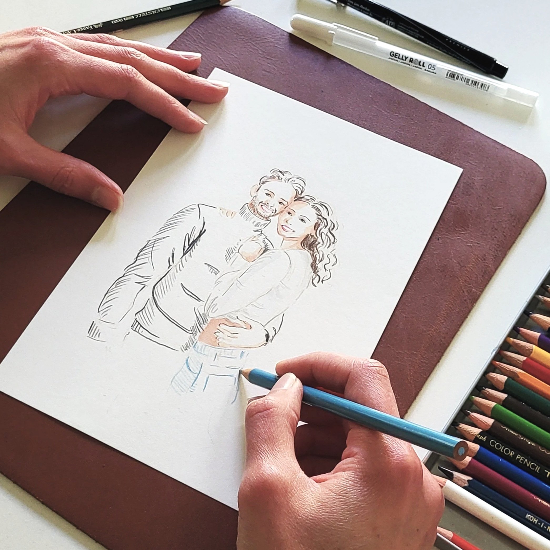 Person coloring a fashion illustration of a couple with colored pencils arranged on a table.