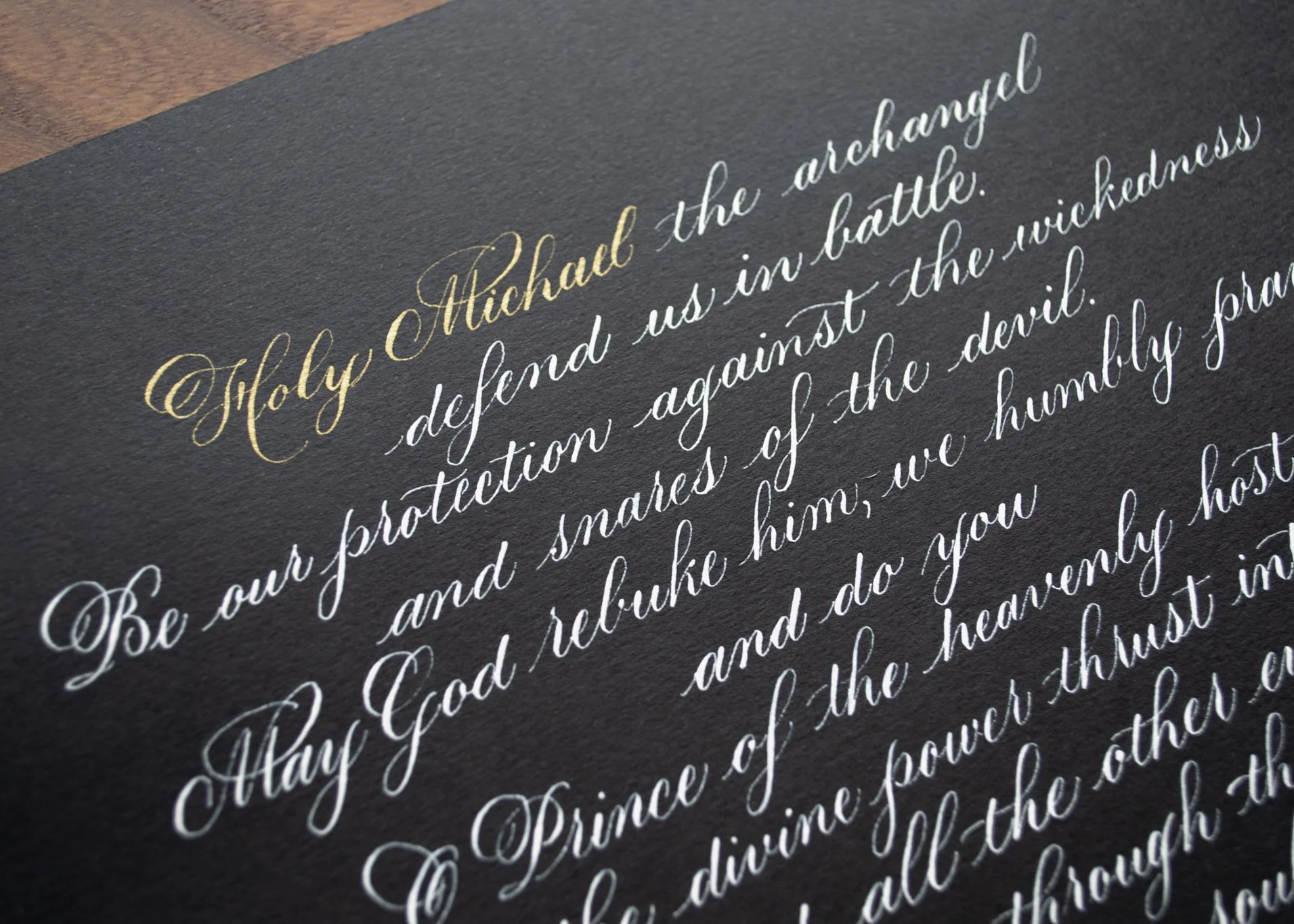 Close-up of a black paper with cursive handwritten text in gold and white ink, quoting from the Bible, Proverbs 31.