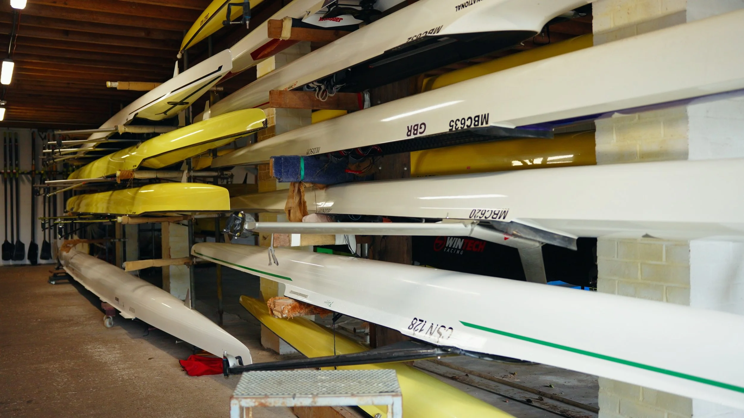 Multiple kayaks and canoes stored horizontally on a rack inside a garage or storage room.