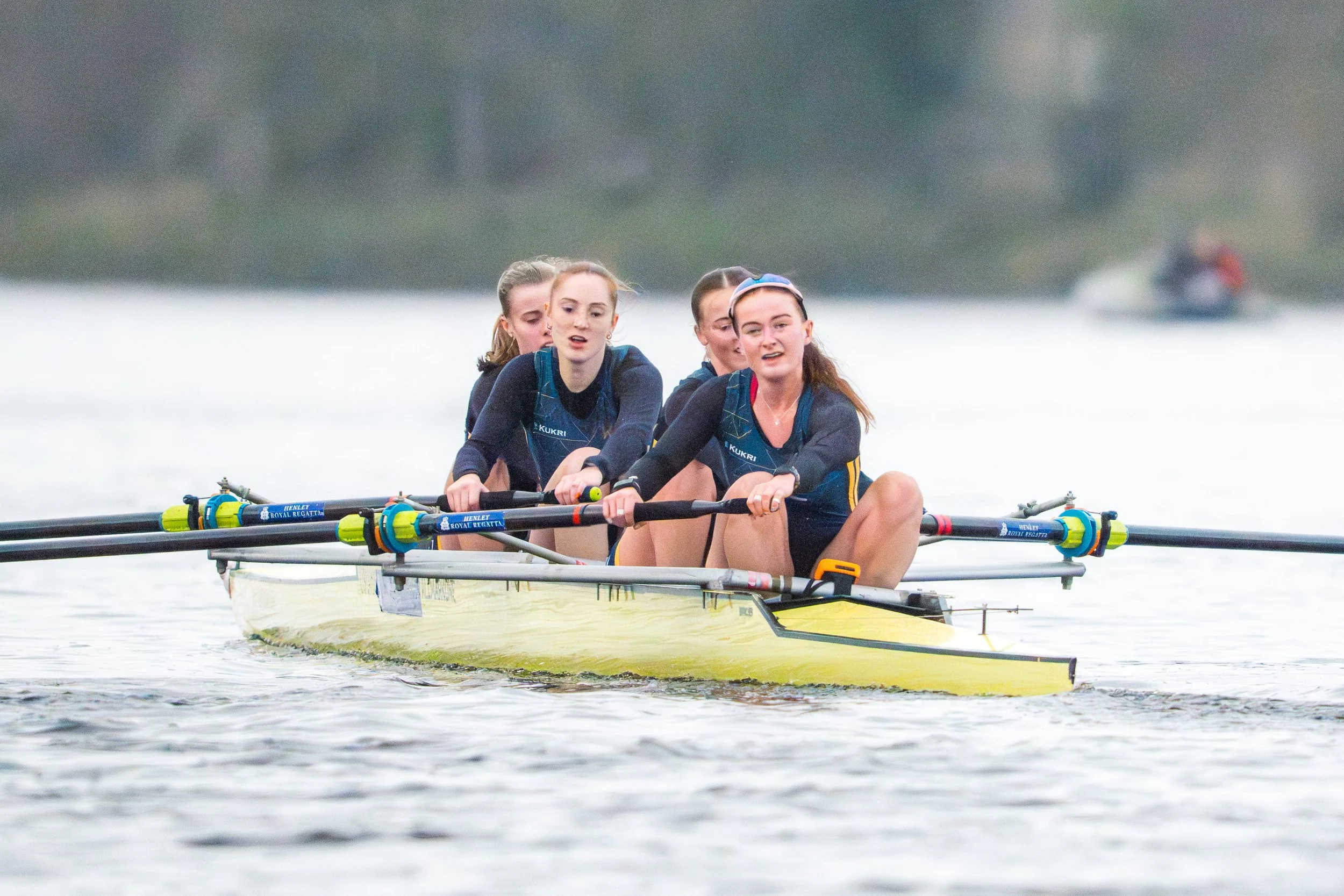 Four women in a rowing shell on a lake, preparing to row.
