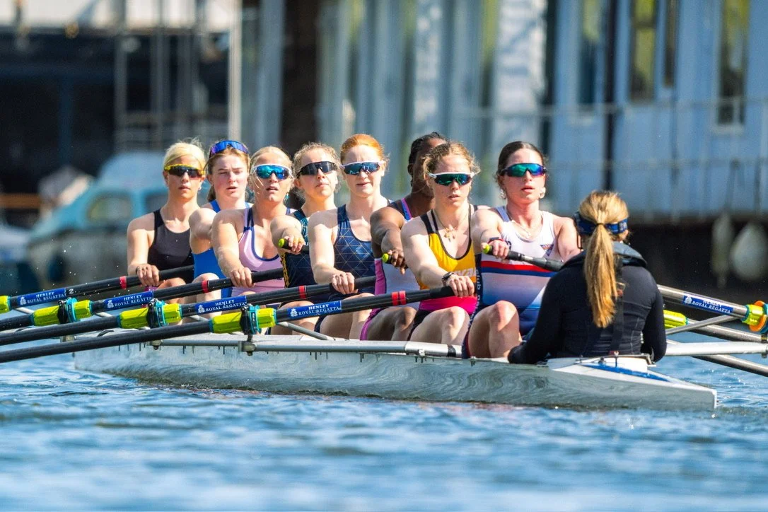 Women's rowing team practicing on the water, wearing sunglasses and athletic uniforms.