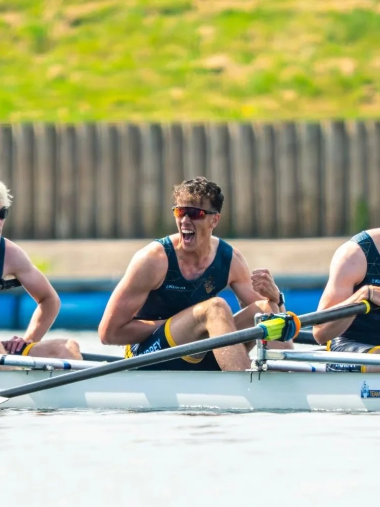 A woman in a rowing boat celebrates with a joyful expression during a rowing competition.