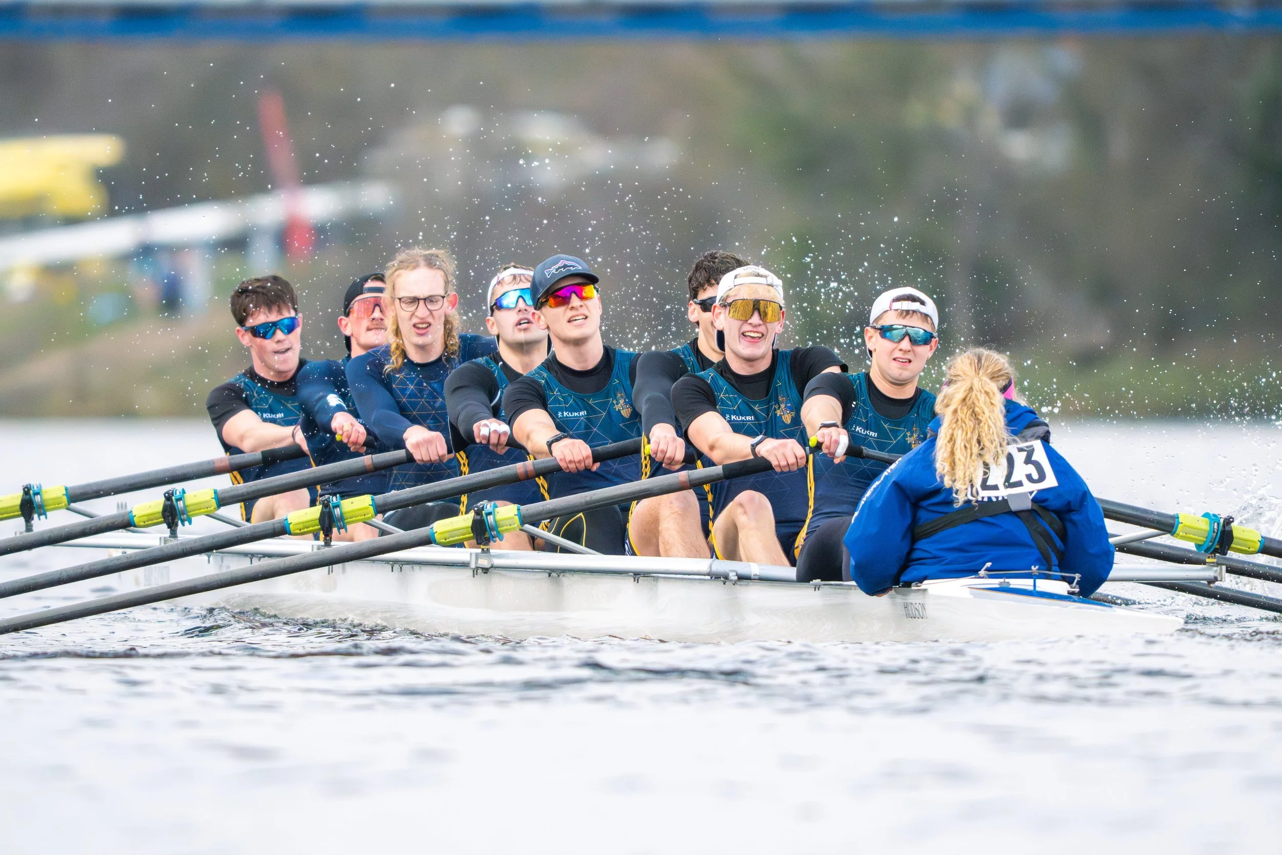 A team of male rowers in blue uniforms competing in a rowing race on a river.