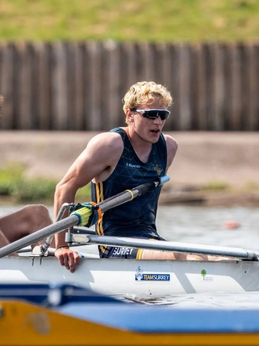 A young man in athletic gear and sunglasses rowing a boat during a race.