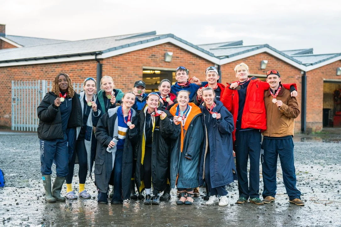 Group of young athletes wearing medals and rain gear, standing outside school building, celebrating their success.
