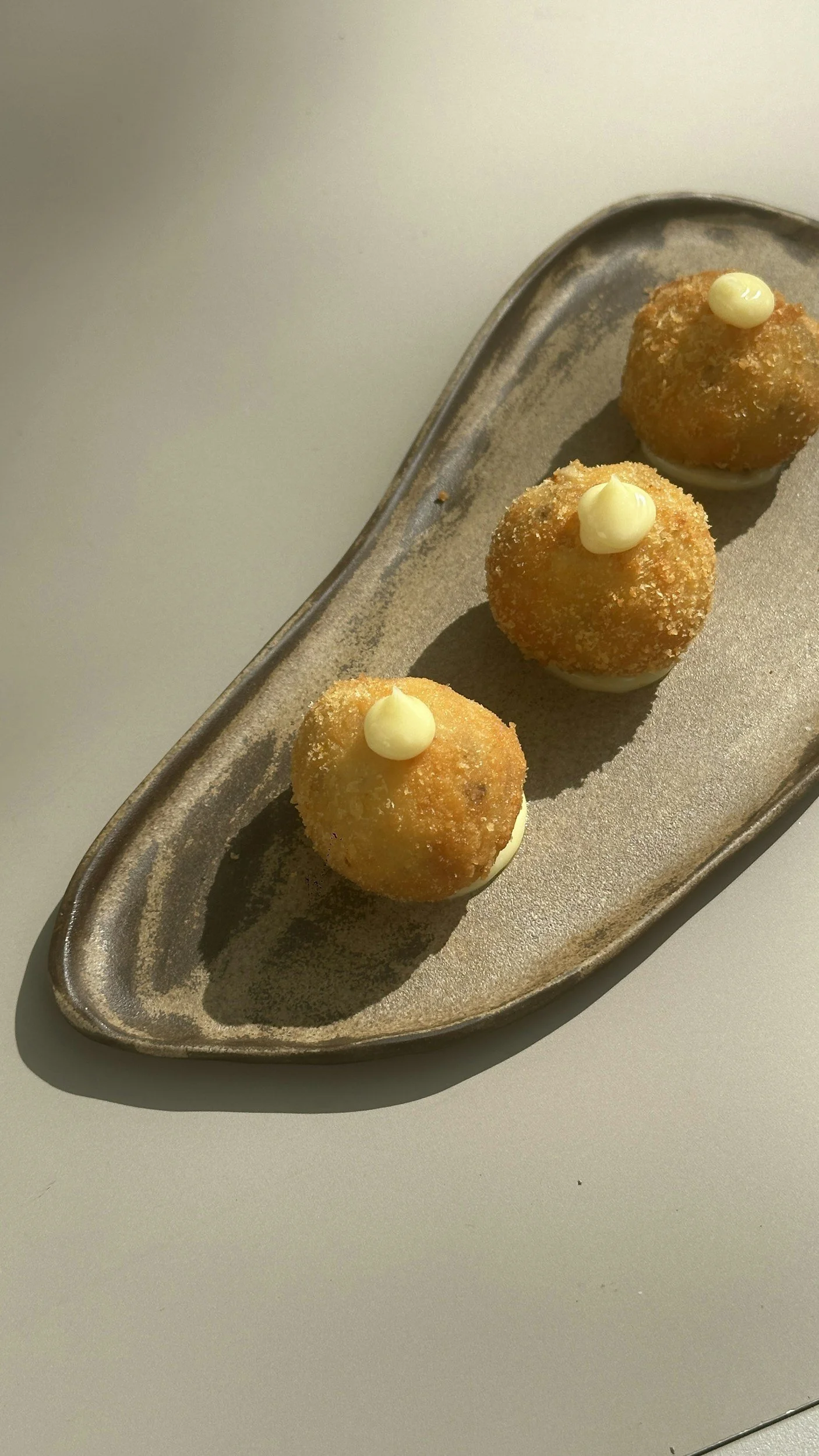 Trois croquettes panées avec une petite touche de mayonnaise sur le dessus, présentées sur une assiette en métal.