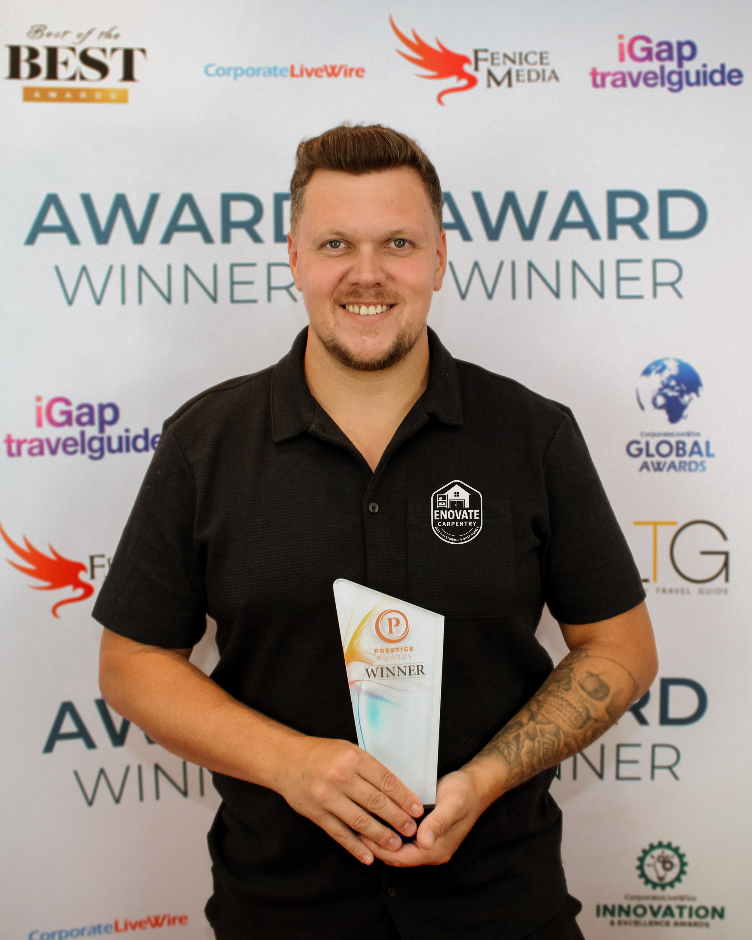 A man with short brown hair and tattoos on his left arm is smiling and holding an award plaque that reads 'Provider Prestige Awards Winner.' He is standing in front of a backdrop with various awards and media logos.