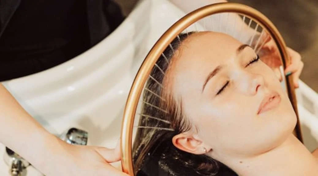 A woman with closed eyes resting her head on a sink's mirror while getting her hair washed.