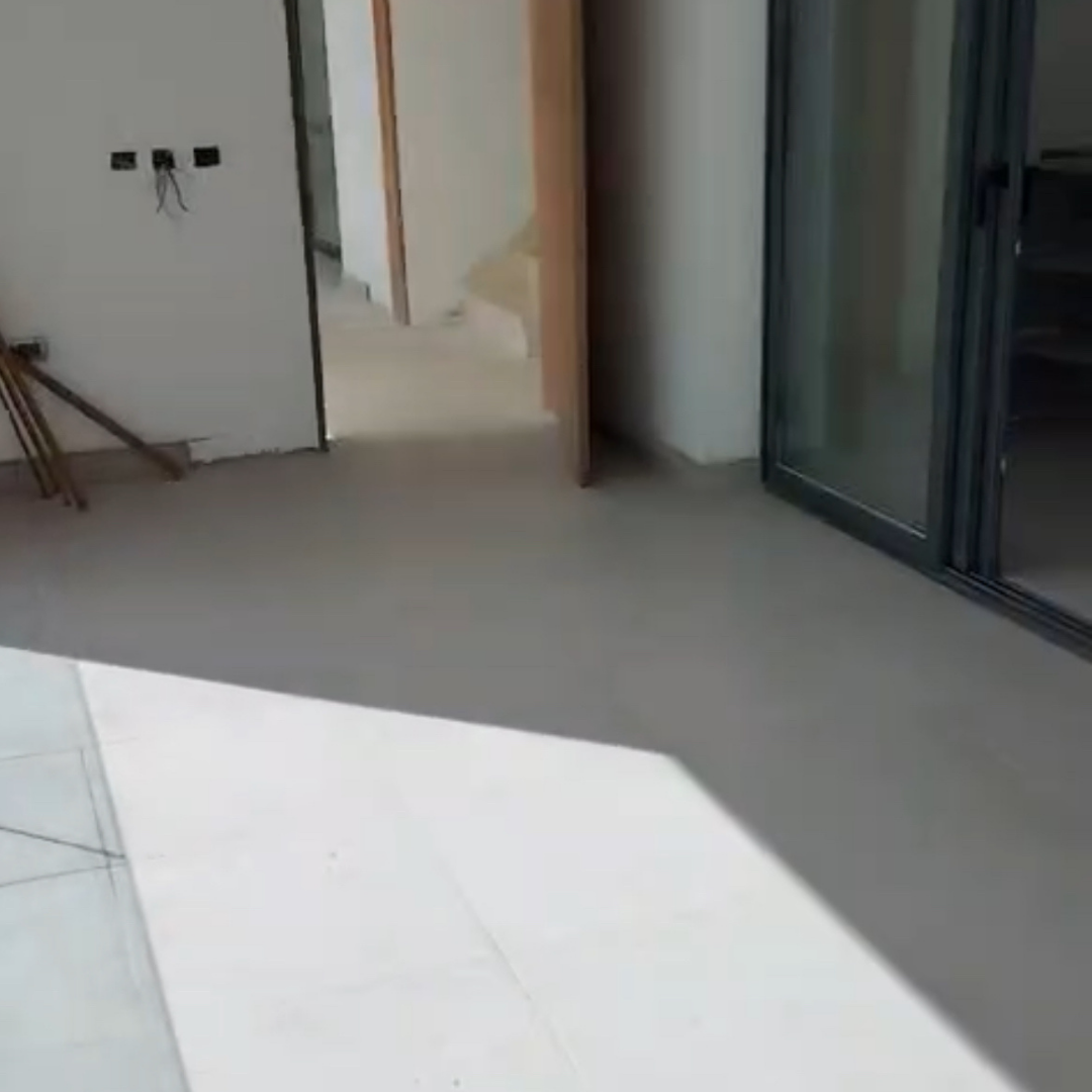Interiores en construcción con paredes sin terminar, un pasillo, un pilar de madera, y un puerta con marco de vidrio.