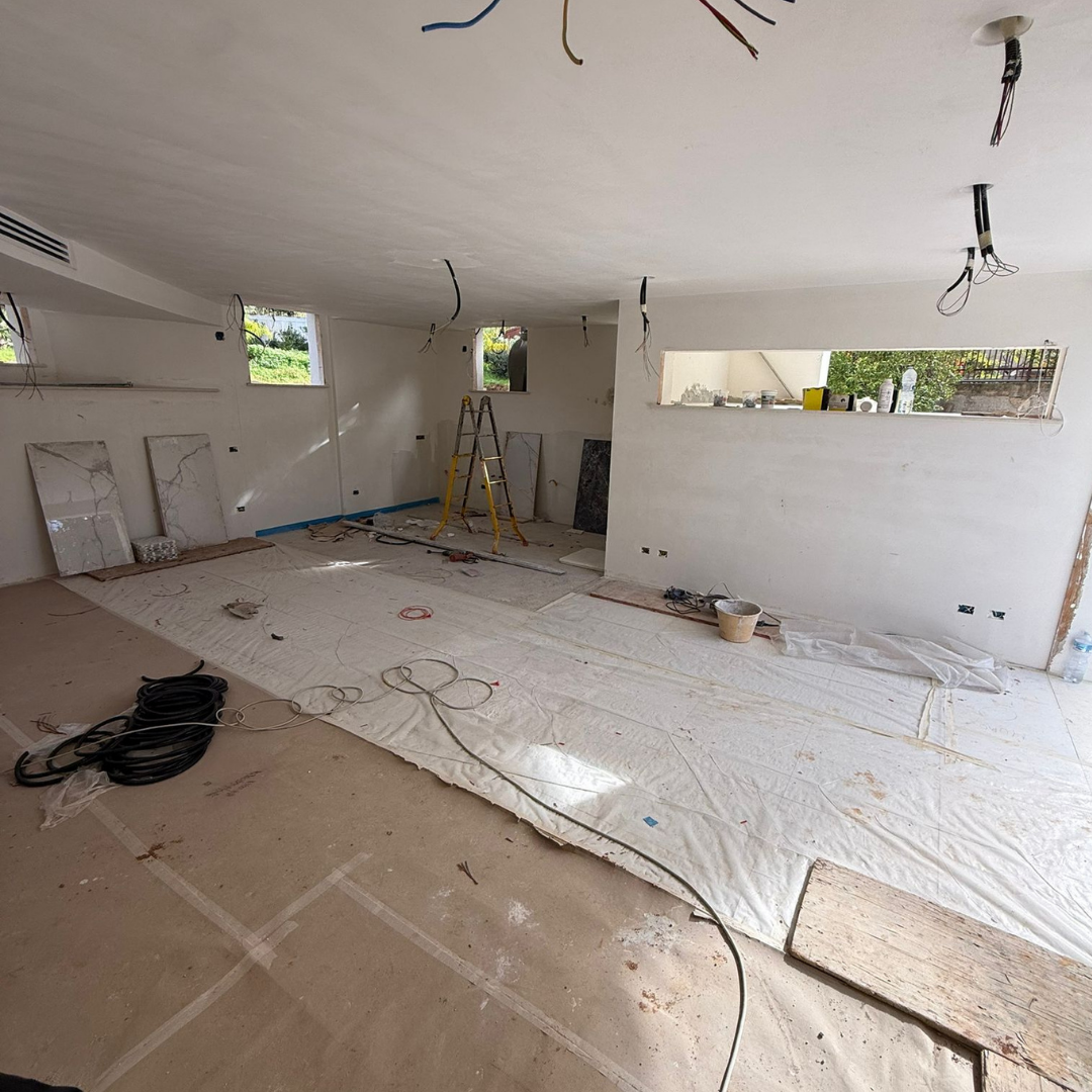 Interiores de una sala en construcción con cables colgando del techo y materiales de construcción en el piso.