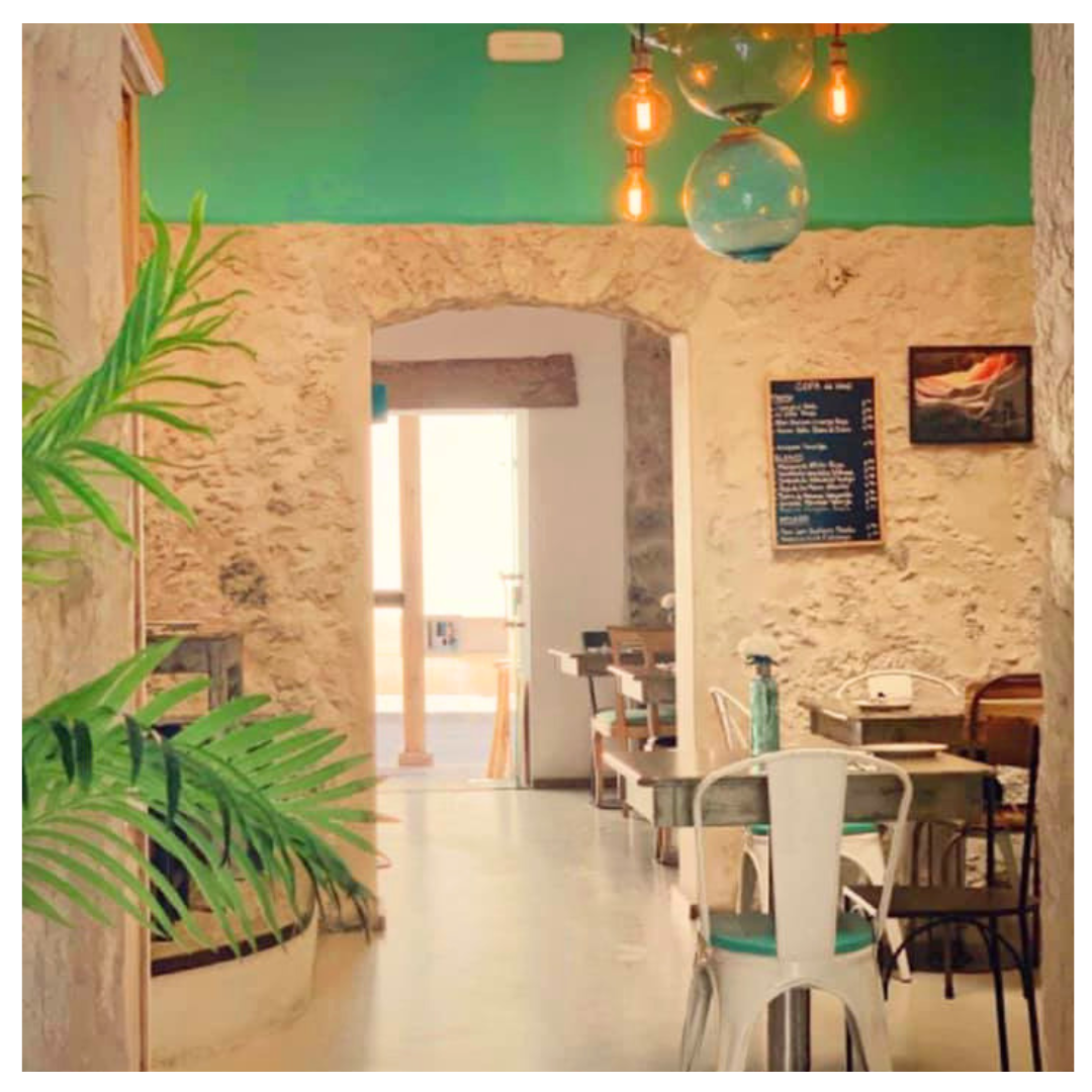 interior de un restaurante con paredes de piedra, mesas y sillas de diferentes estilos, plantas decorativas, un cartel de menú en la pared y una lámpara colgante