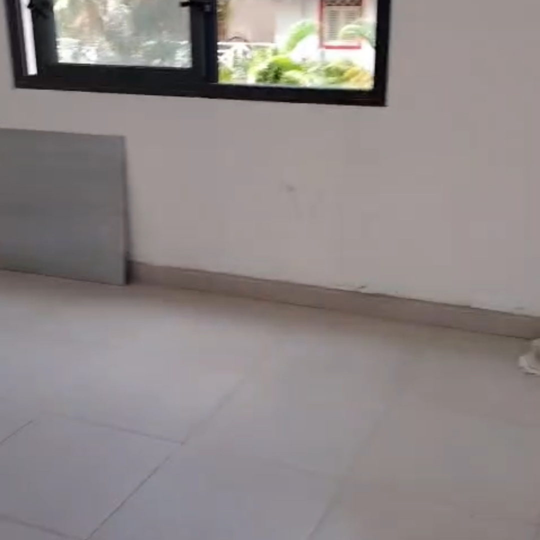 Interior de una habitación vacía con piso de baldosas y una ventana abierta, con algunas plantas visibles afuera.