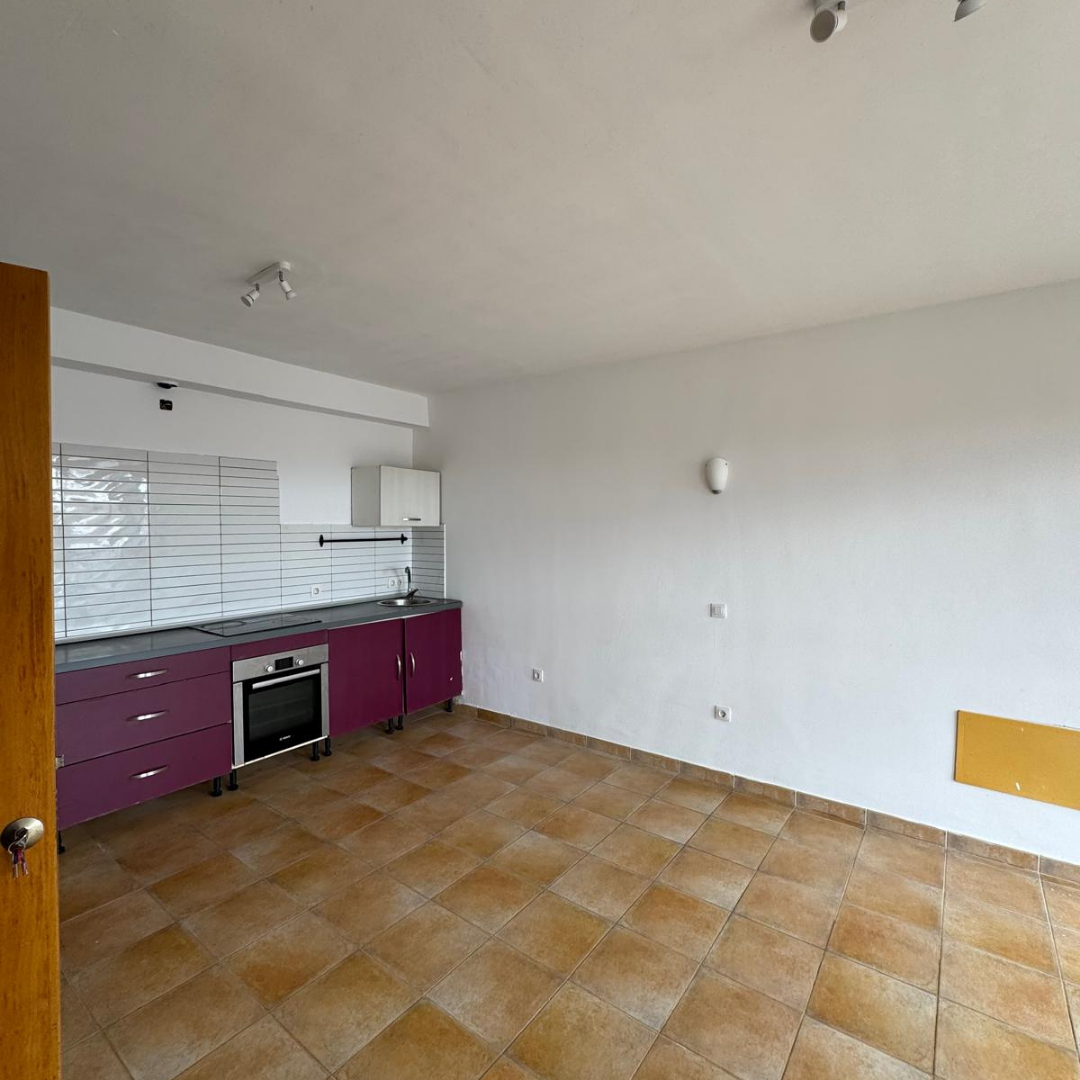 Cocina vacía con gabinetes morados, encimera gris, pared de azulejos grises y piso de baldosas marrones.