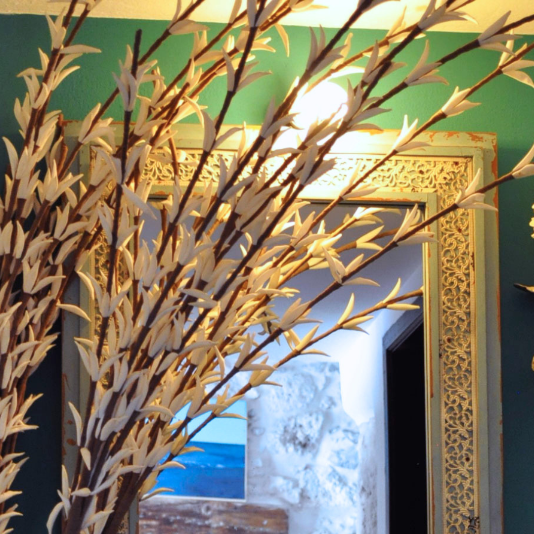 Ramas secas decorativas en primer plano en un interior con un espejo decorativo y paredes verdes.