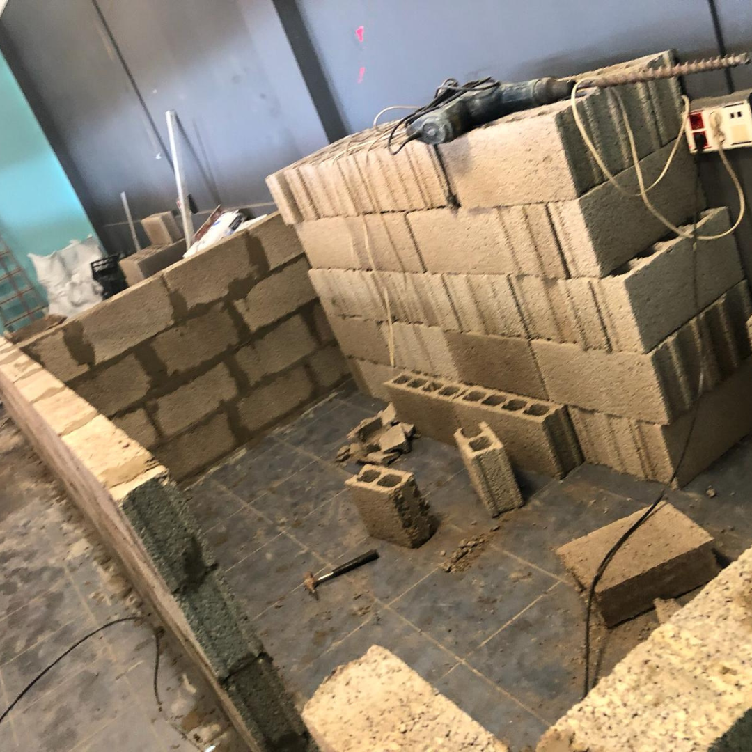 Construcción de una pared con bloques de cemento en interior, con herramientas y cables sobre el suelo de baldosas.
