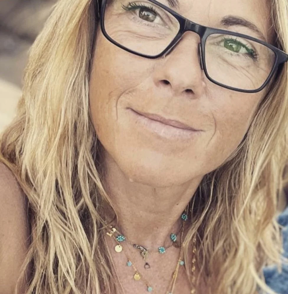 Retrato de una mujer con gafas negras, cabello rubio, y varias cadenas con collares de diferentes colores.