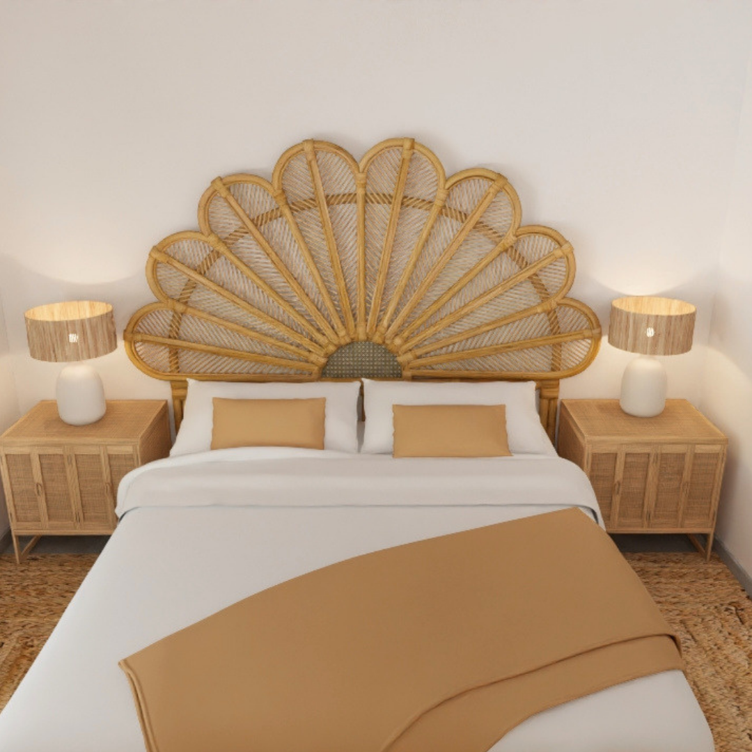 Cama doble con cabecera de mimbre en forma de concha, con dos mesas de noche a ambos lados, cada una con una lámpara de mesa. La cama tiene sábanas blancas y almohadas beige.