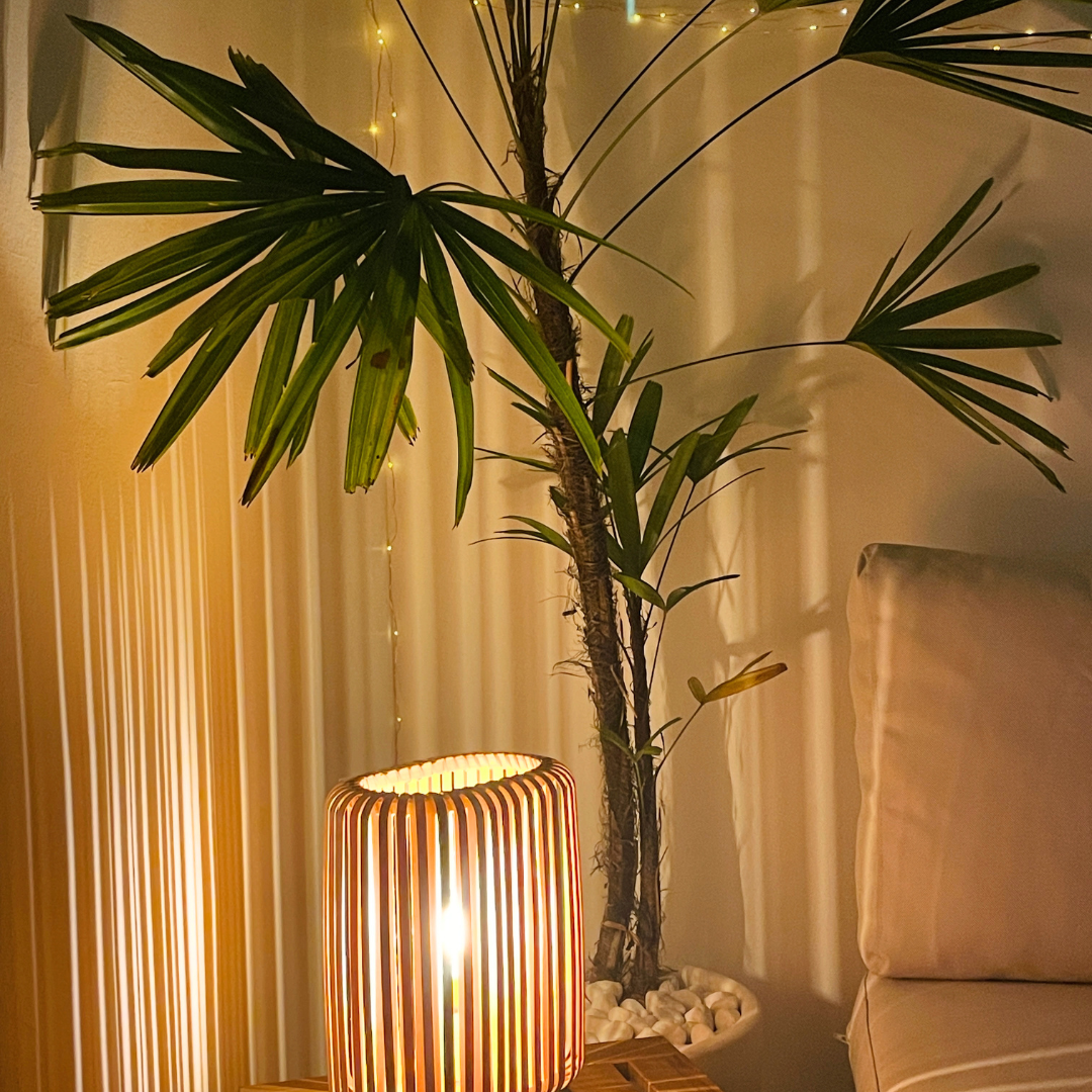 Una lámpara de madera en una habitación con una planta de interior y cortinas blancas, decorada con luces.