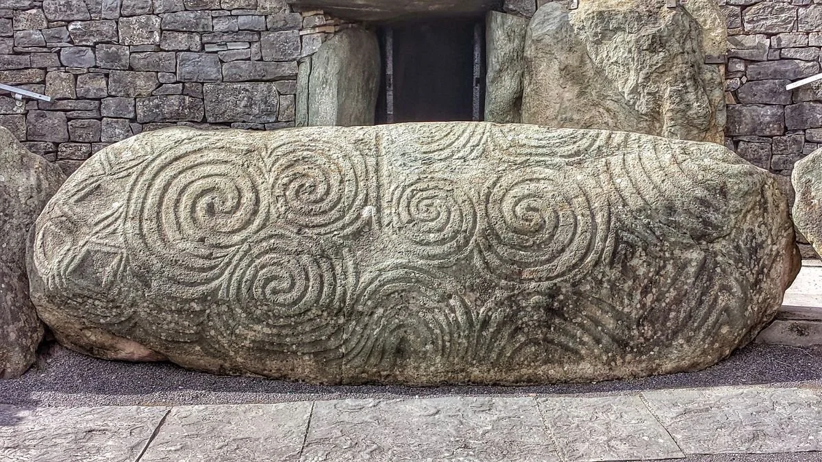 Grande pietra con incisioni a spirale e linee ondulate, probabile manufatto preistorico o storico.