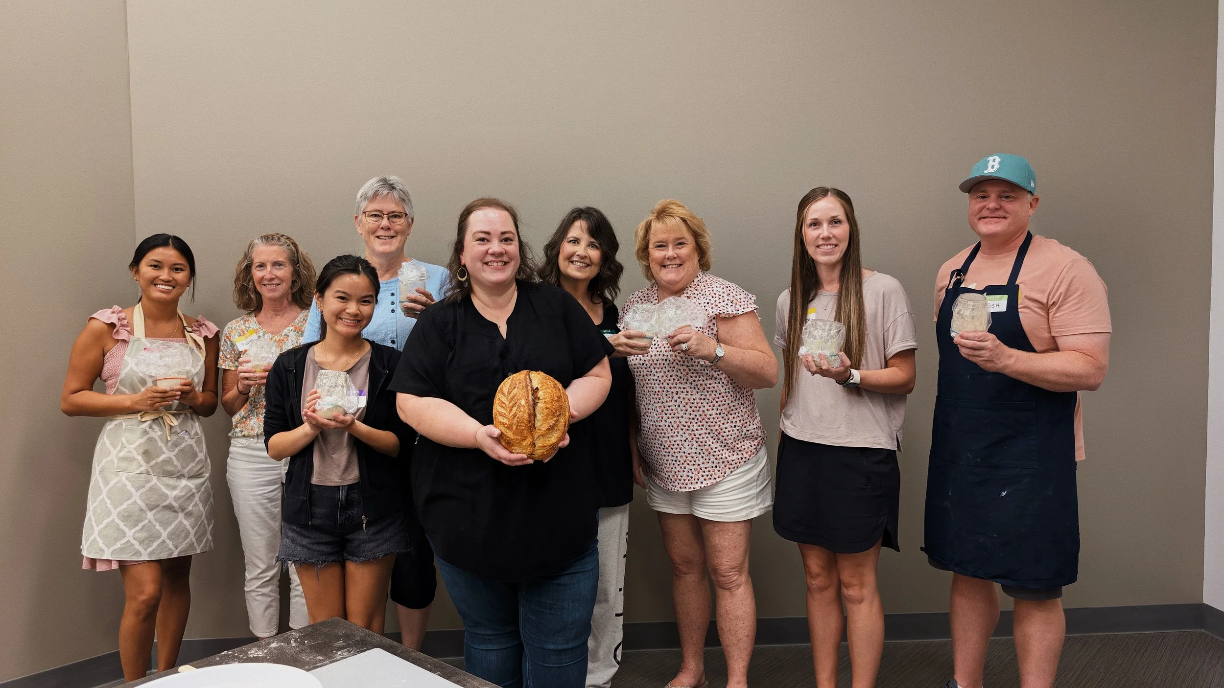 Group of workshop attendees, smiling at the camera and holding glass jars with sourdough starter.
