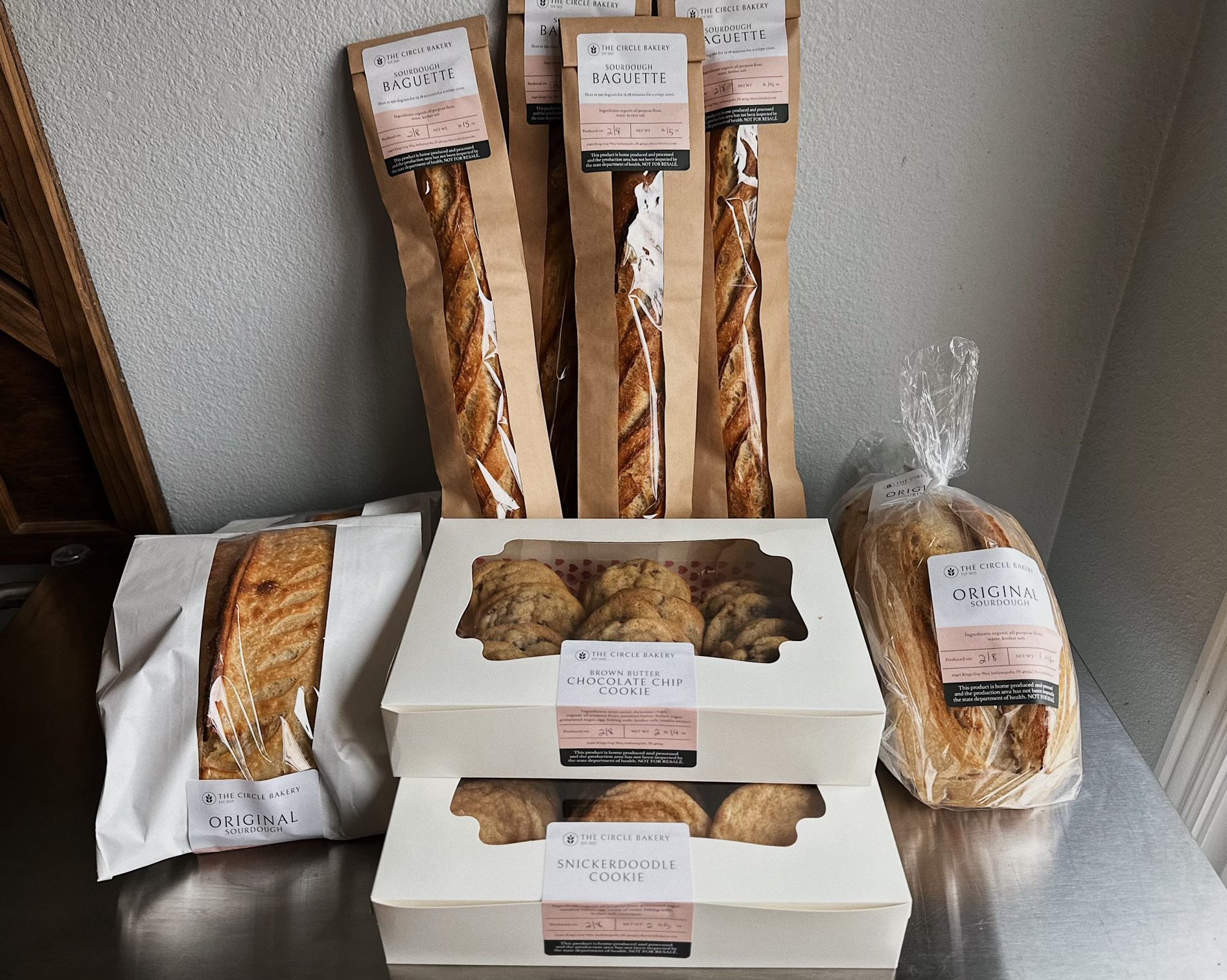 Several packages of sourdough baked goods, including baguettes, and cookies from The Circle Bakery, arranged on a table against a wall.